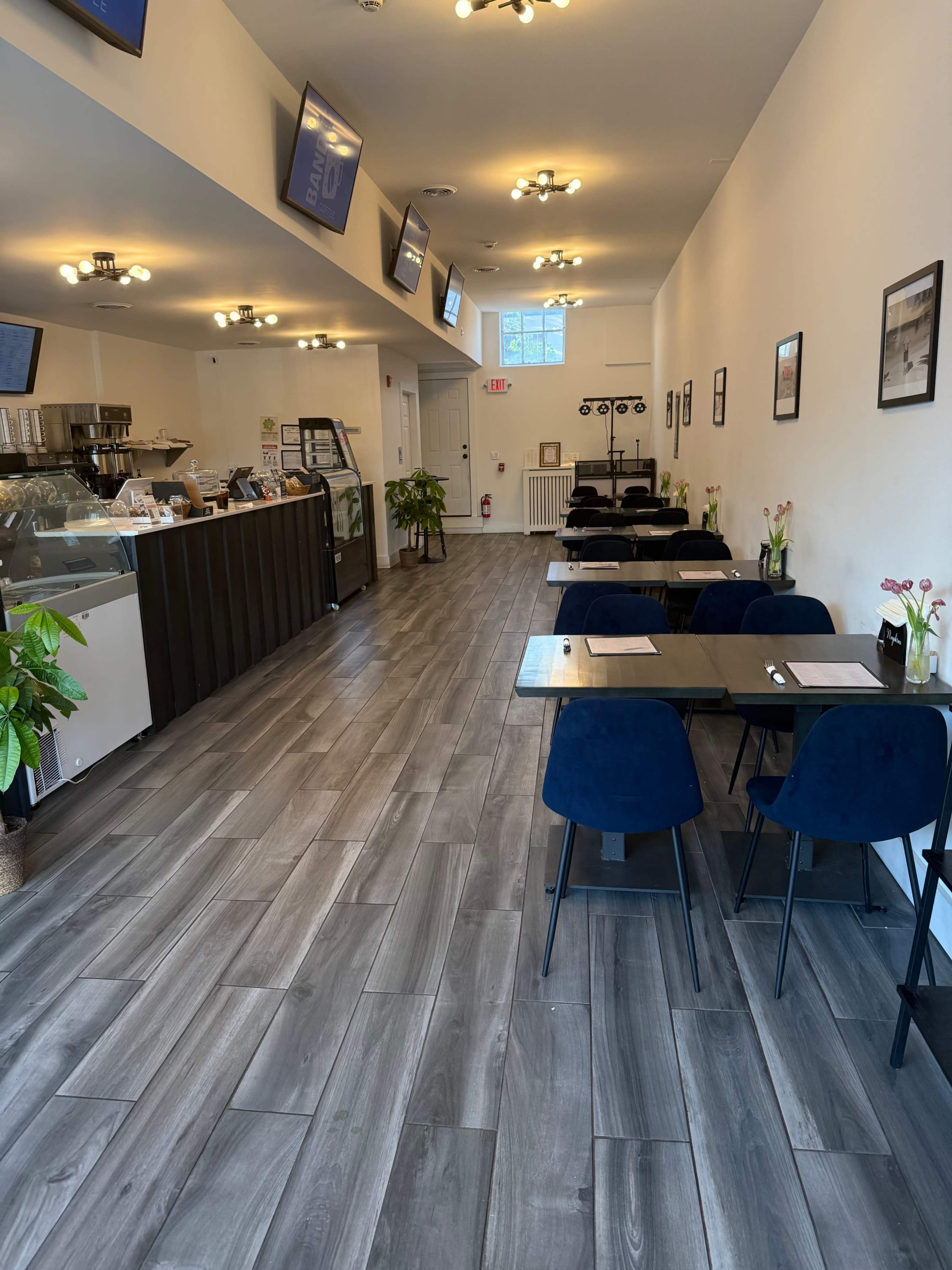 The image shows a spacious café interior with a counter displaying desserts and several tables arranged for dining, illuminated by overhead lights.
