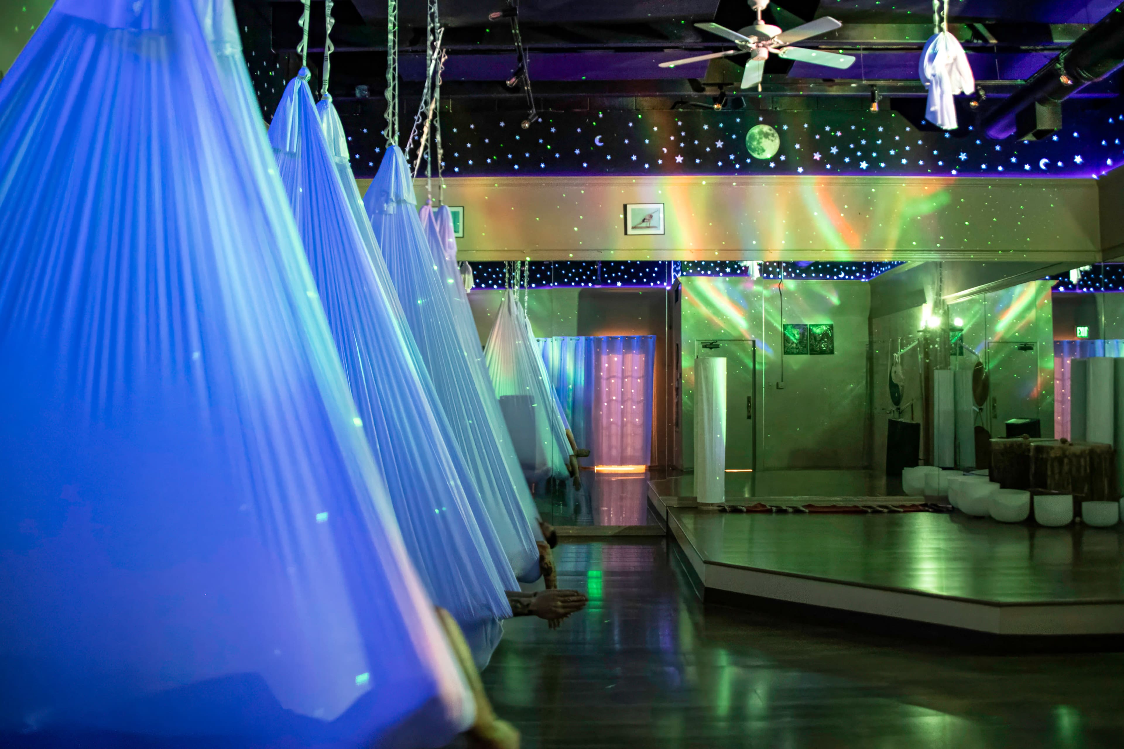 The indoor space features suspended fabric hammocks under colorful lighting, with reflective surfaces and a starry ceiling design.