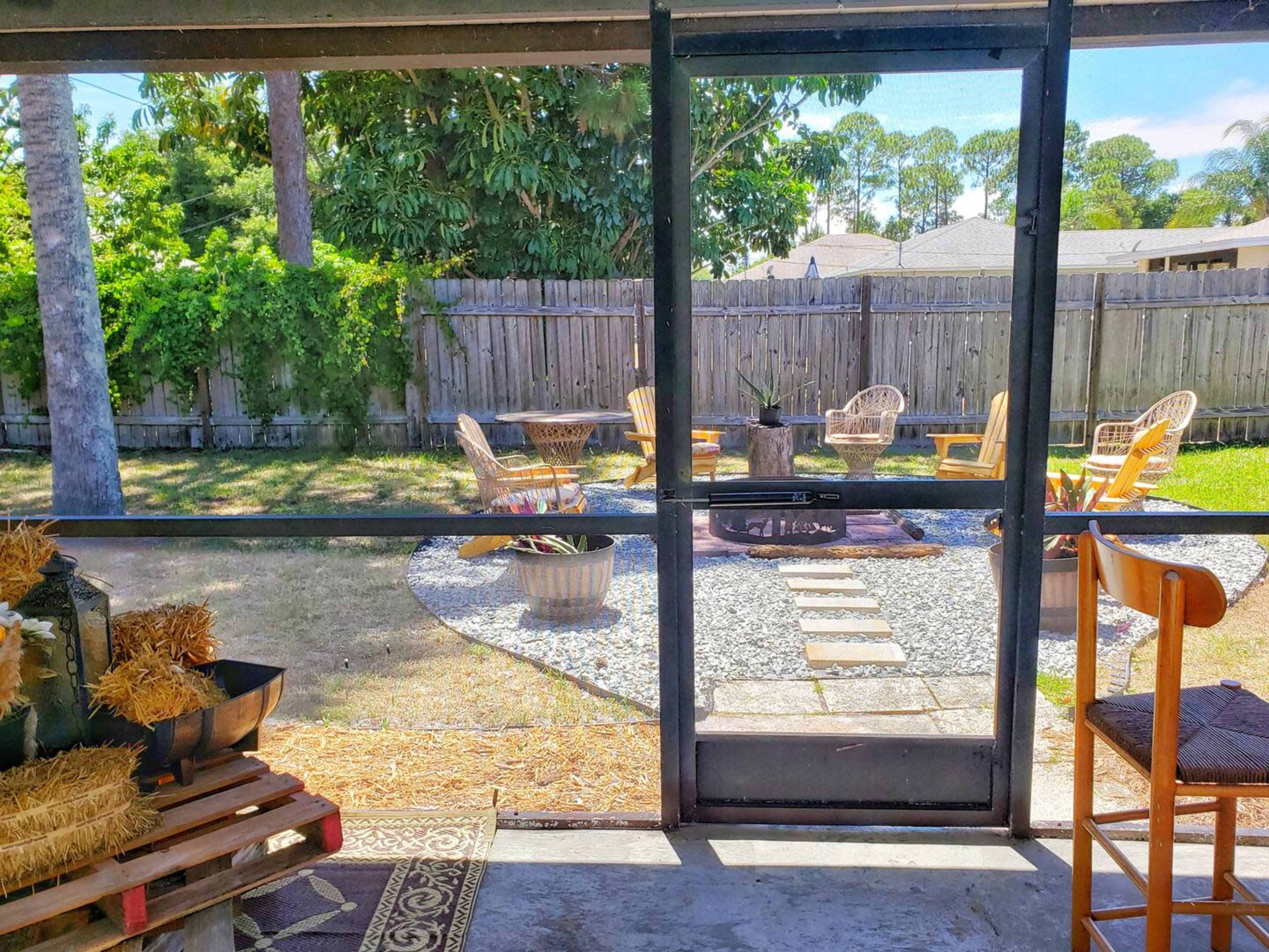 A backyard with a gravel fire pit area surrounded by chairs, framed by a screened porch.