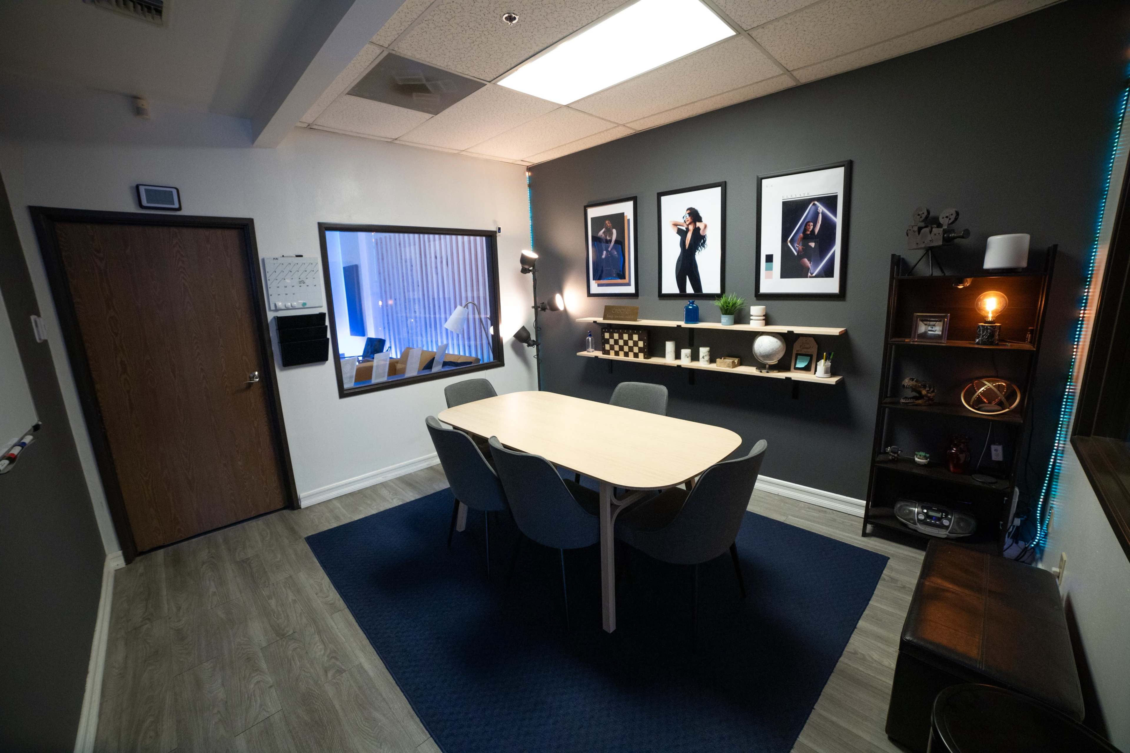 A modern conference room with a round table surrounded by chairs, framed photographs on the walls, and a shelf displaying decorative items.