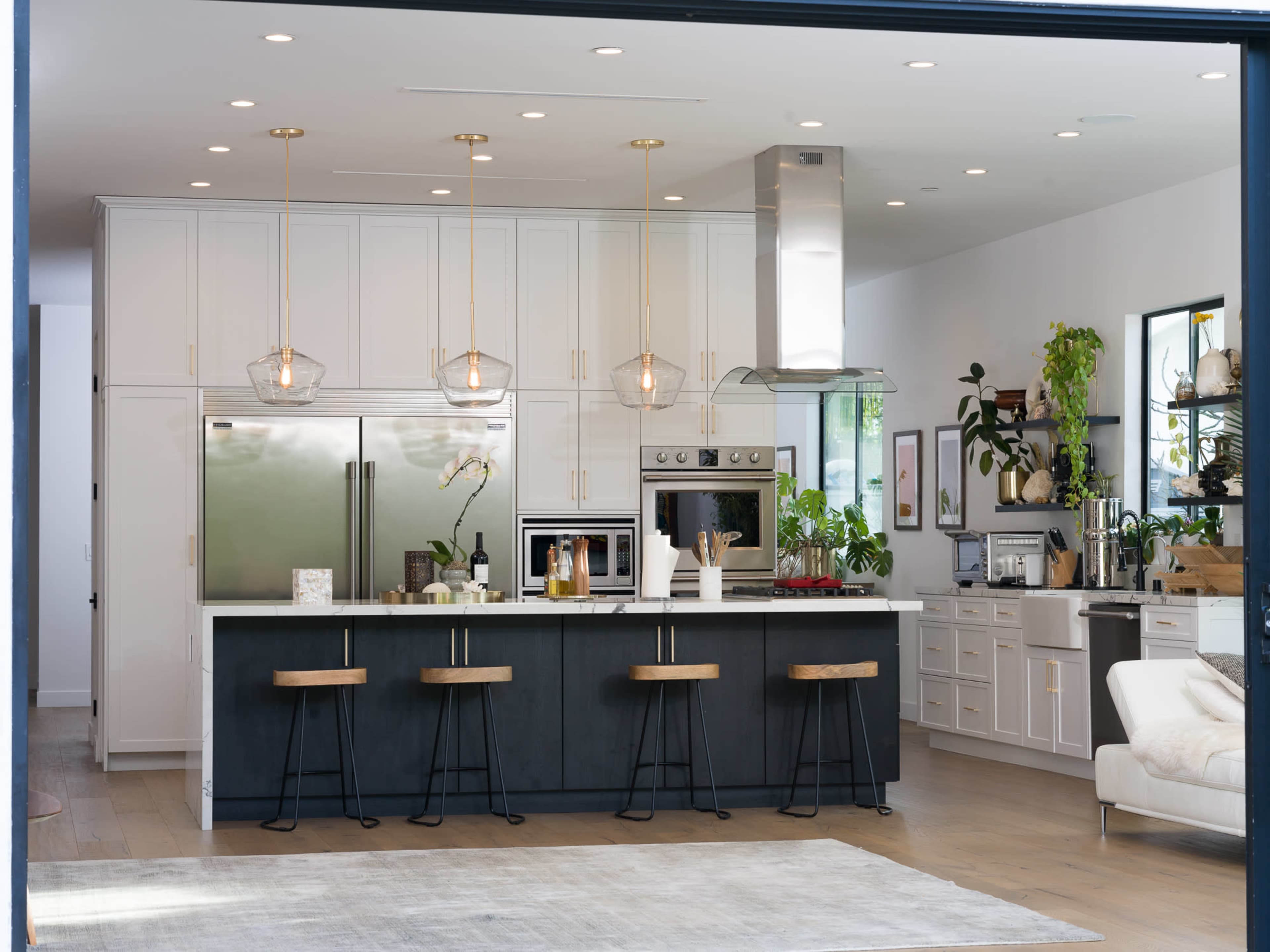A modern kitchen features a central island with bar stools, sleek white cabinetry, and stainless steel appliances.