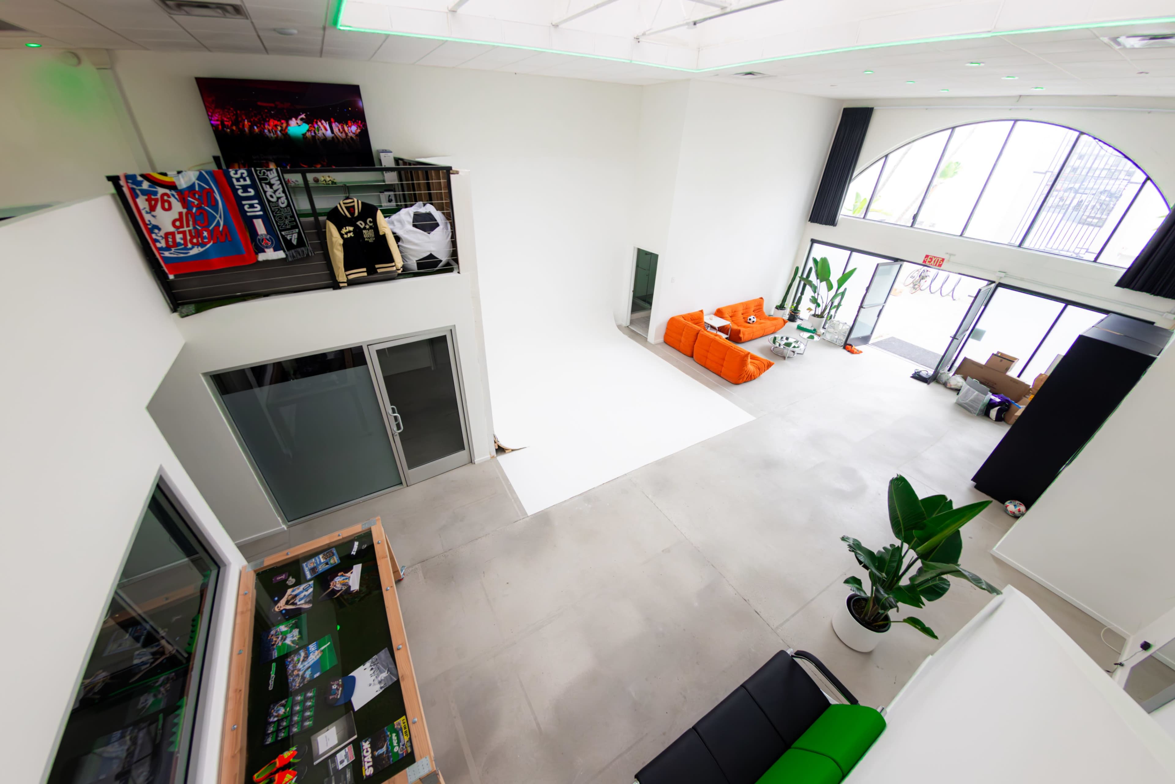 A spacious, modern interior with a white wall, large windows, an orange couch, and a display area featuring various items.