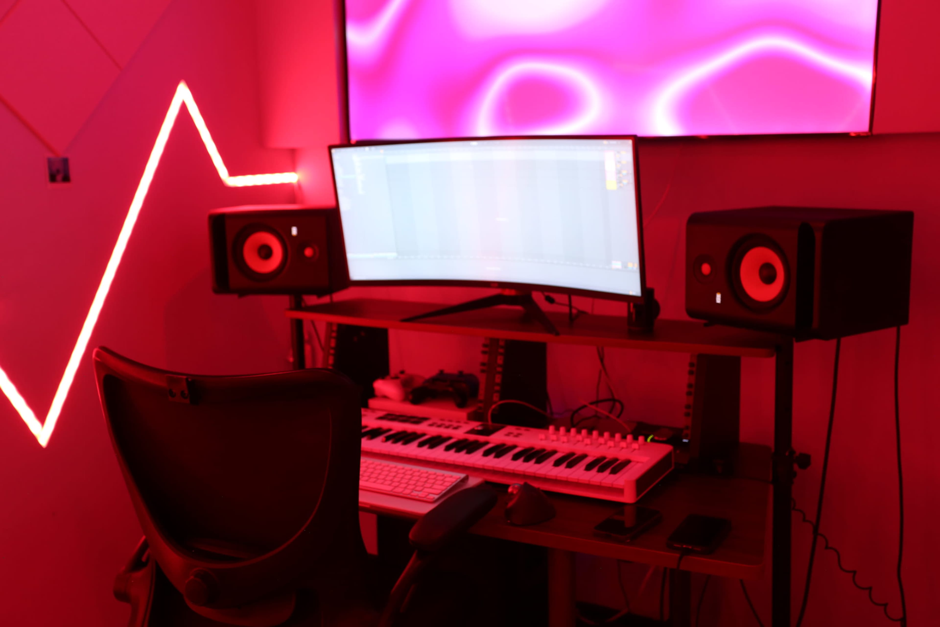 A music production setup features a keyboard, computer monitor, and speakers, illuminated by red LED lights.