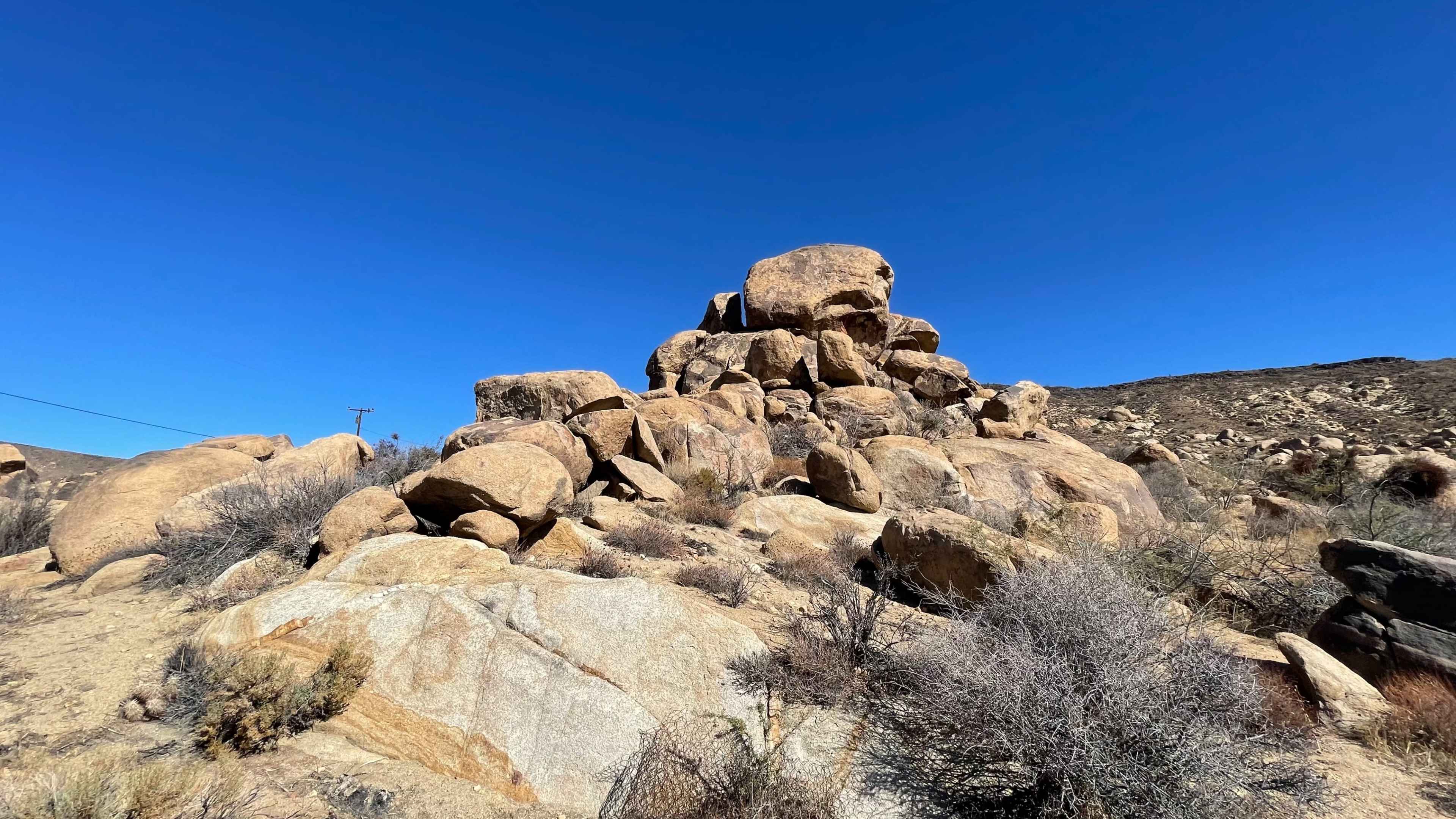 A cluster of large, rugged boulders rises from a desert landscape under a clear blue sky.