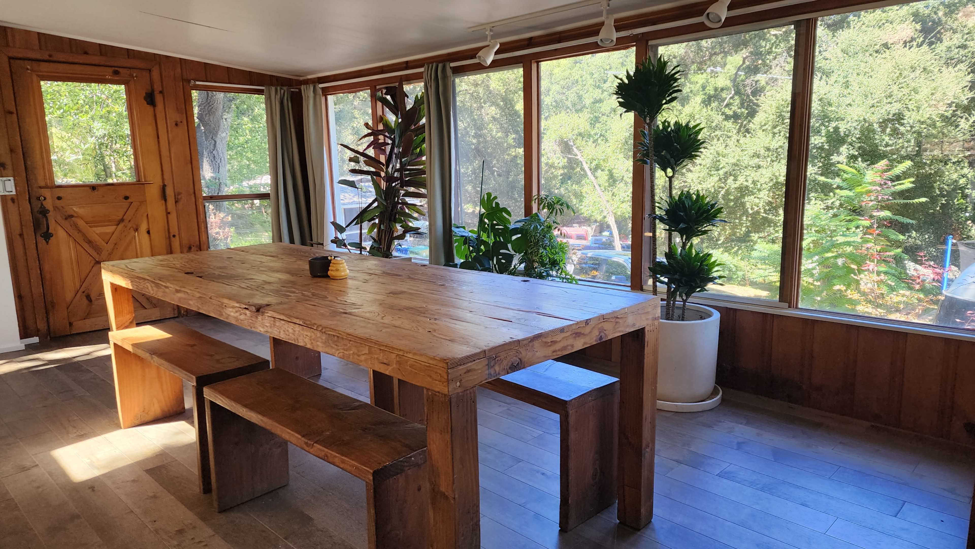 The image shows a wooden table and benches in a well-lit room with large windows overlooking greenery.