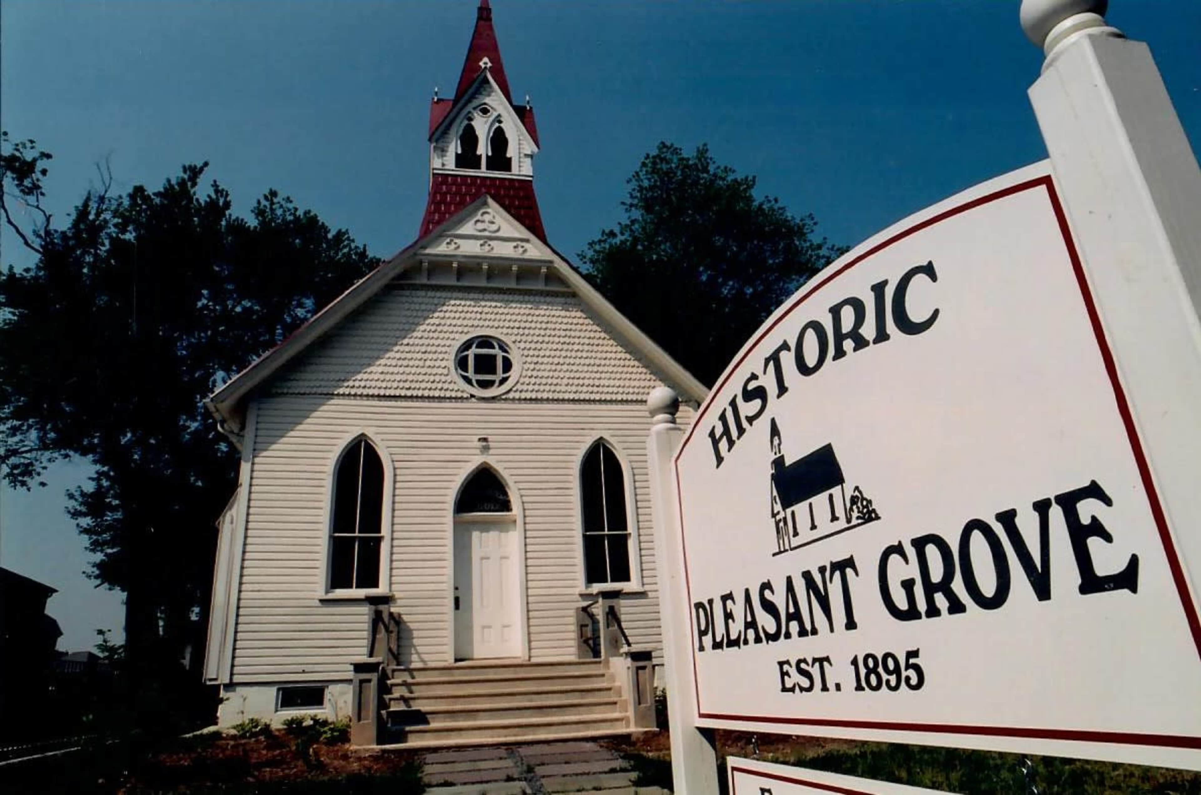 The image shows a historic church with a pointed steeple, accompanied by a sign that reads "Historic Pleasant Grove Est. 1895."