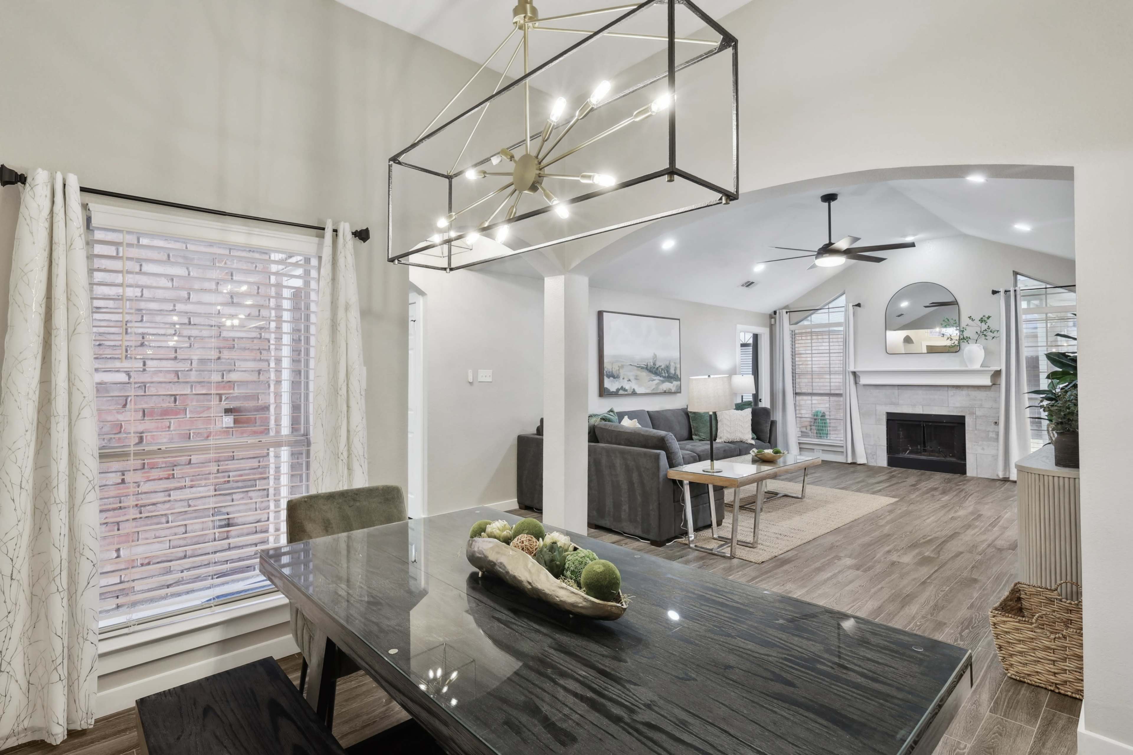 A modern dining area features a black dining table with a decorative centerpiece, overlooking a living room with a gray sofa and a fireplace.