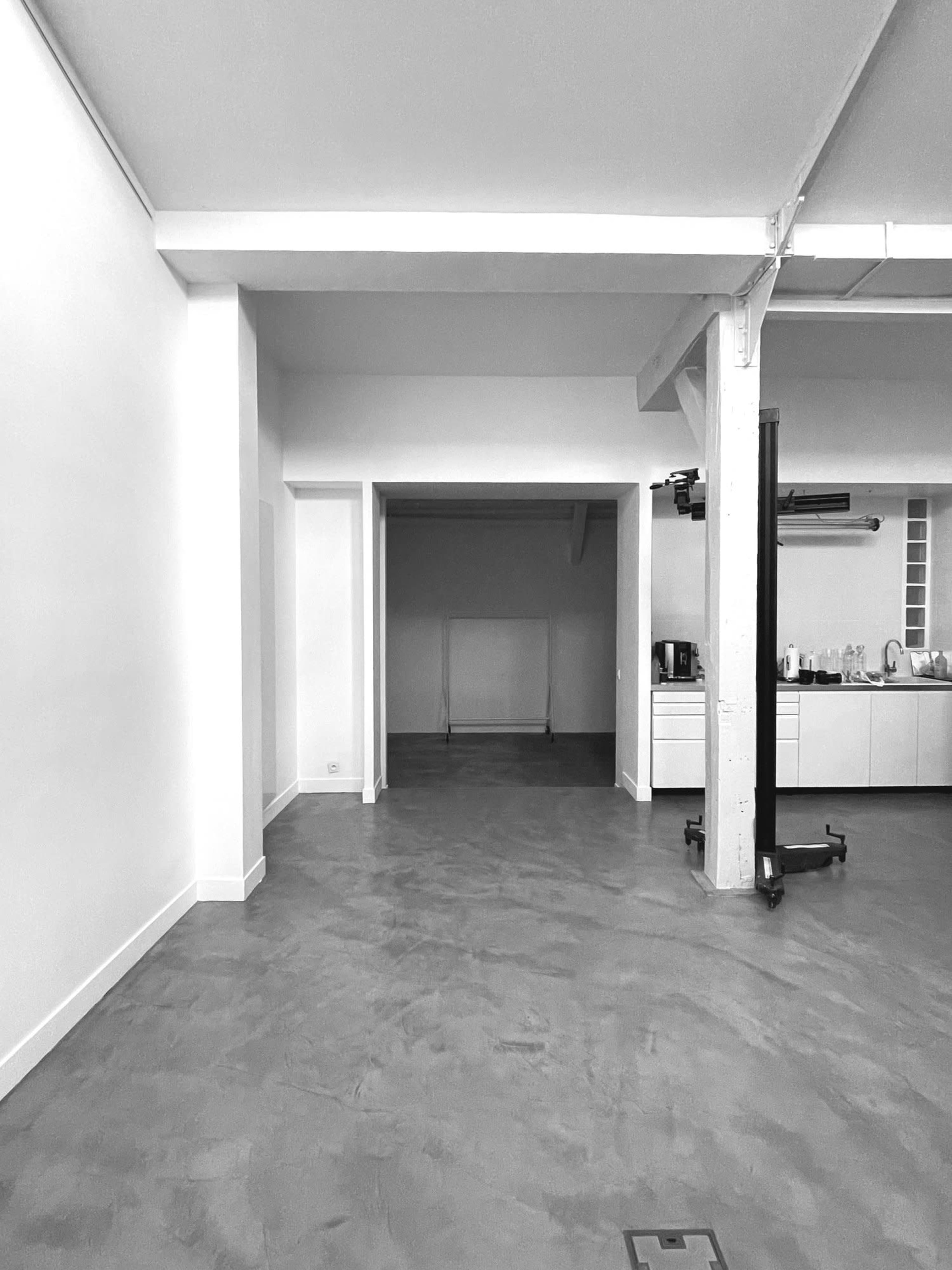 A spacious, empty room with concrete flooring and white walls, featuring an open doorway leading to another area.