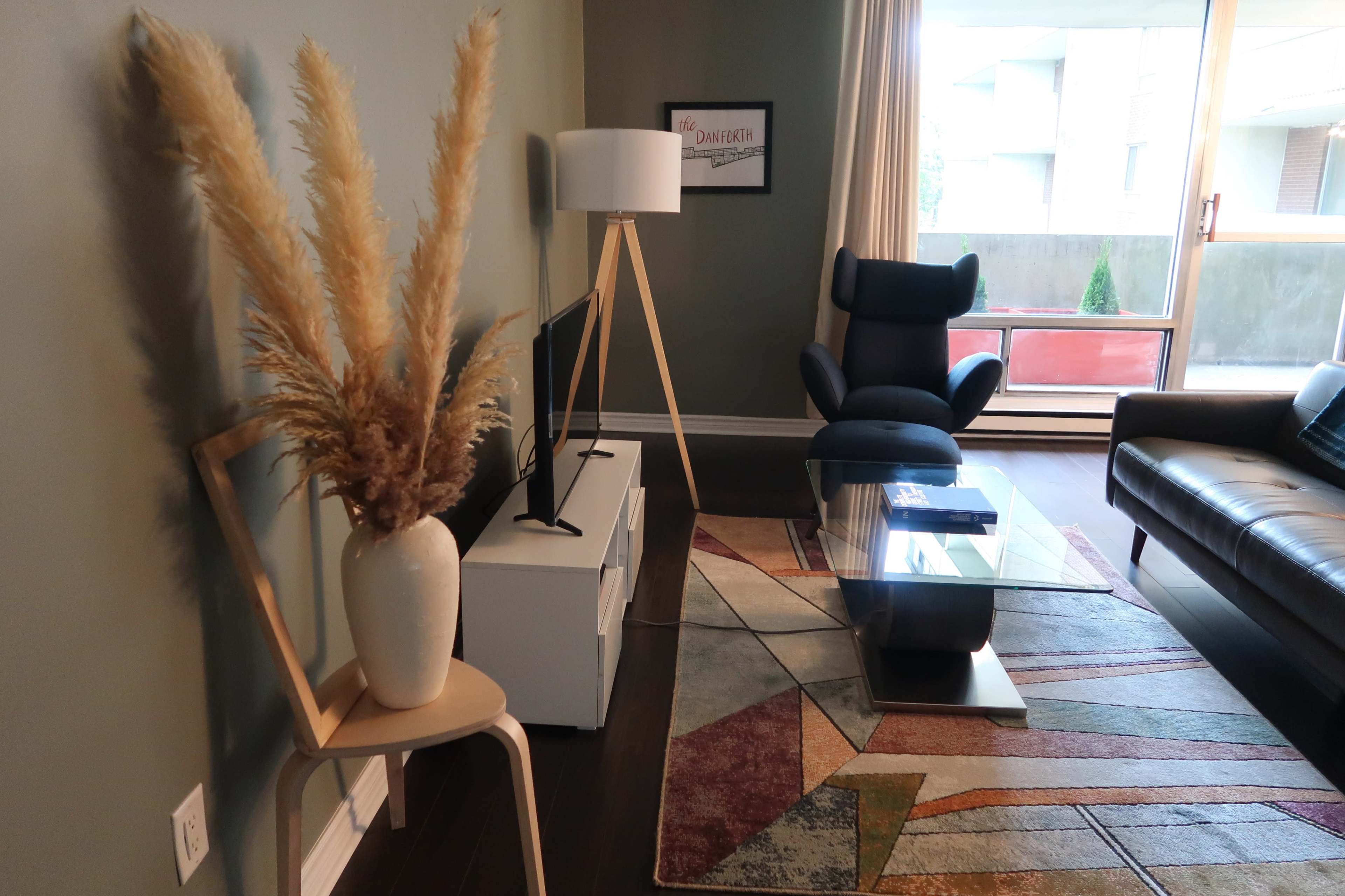 A living room with a modern design featuring a television, a glass coffee table, a comfortable chair, and decorative plants.