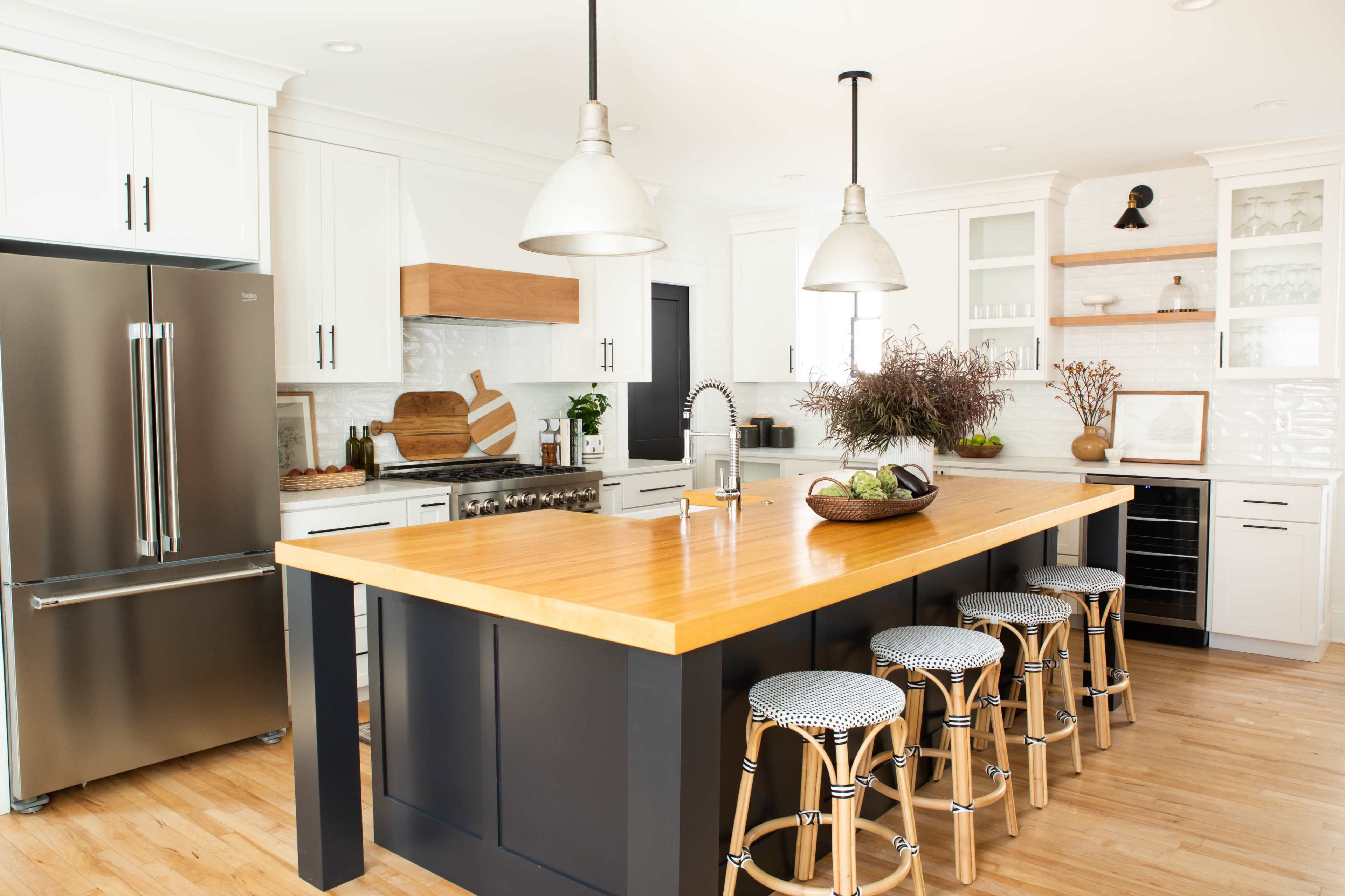 A modern kitchen features a large wooden island with bar stools, stainless steel appliances, and white cabinetry.