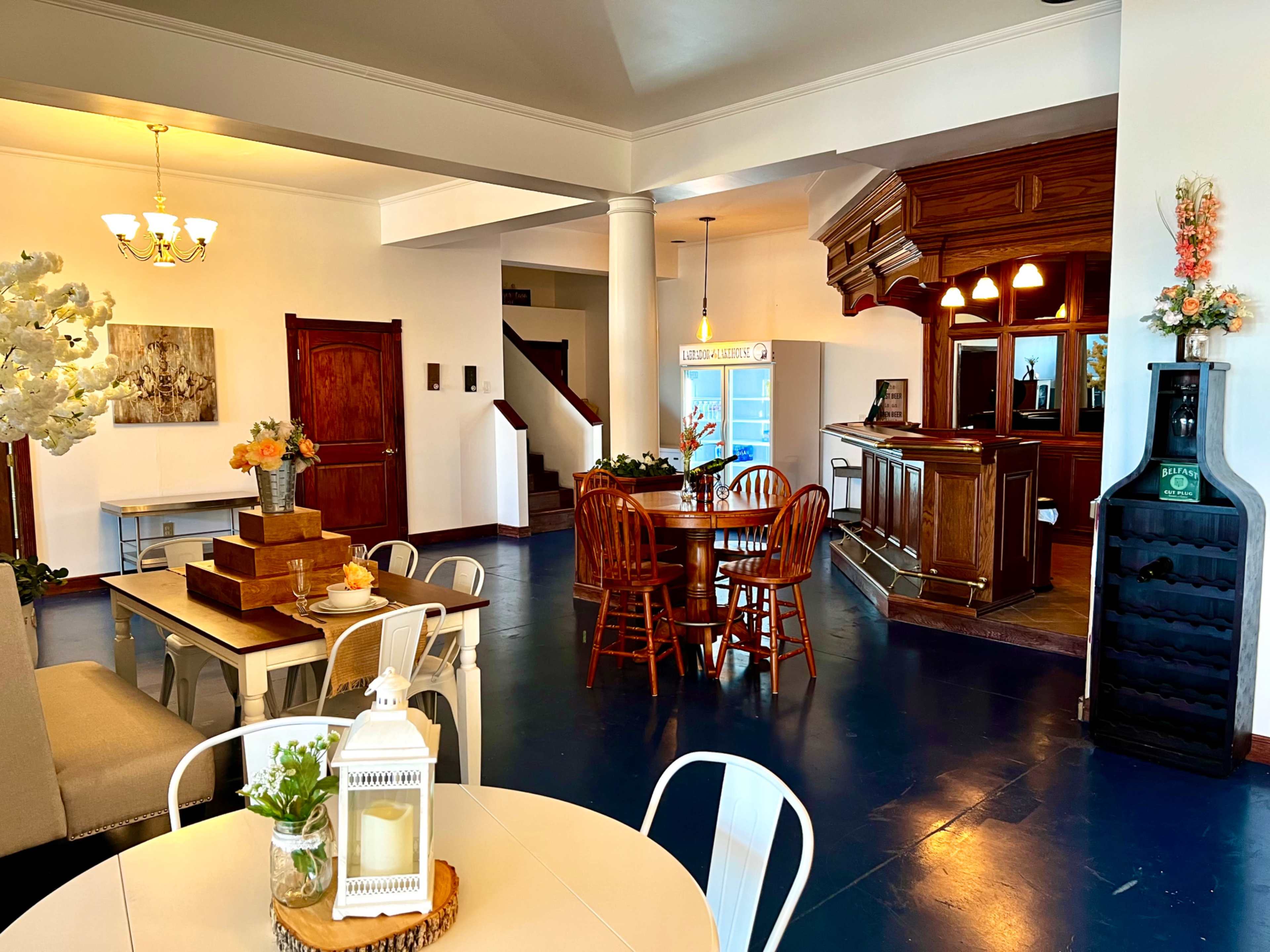 A spacious room features a dining area with wooden chairs around a circular table, a bar counter, and various decorative elements.