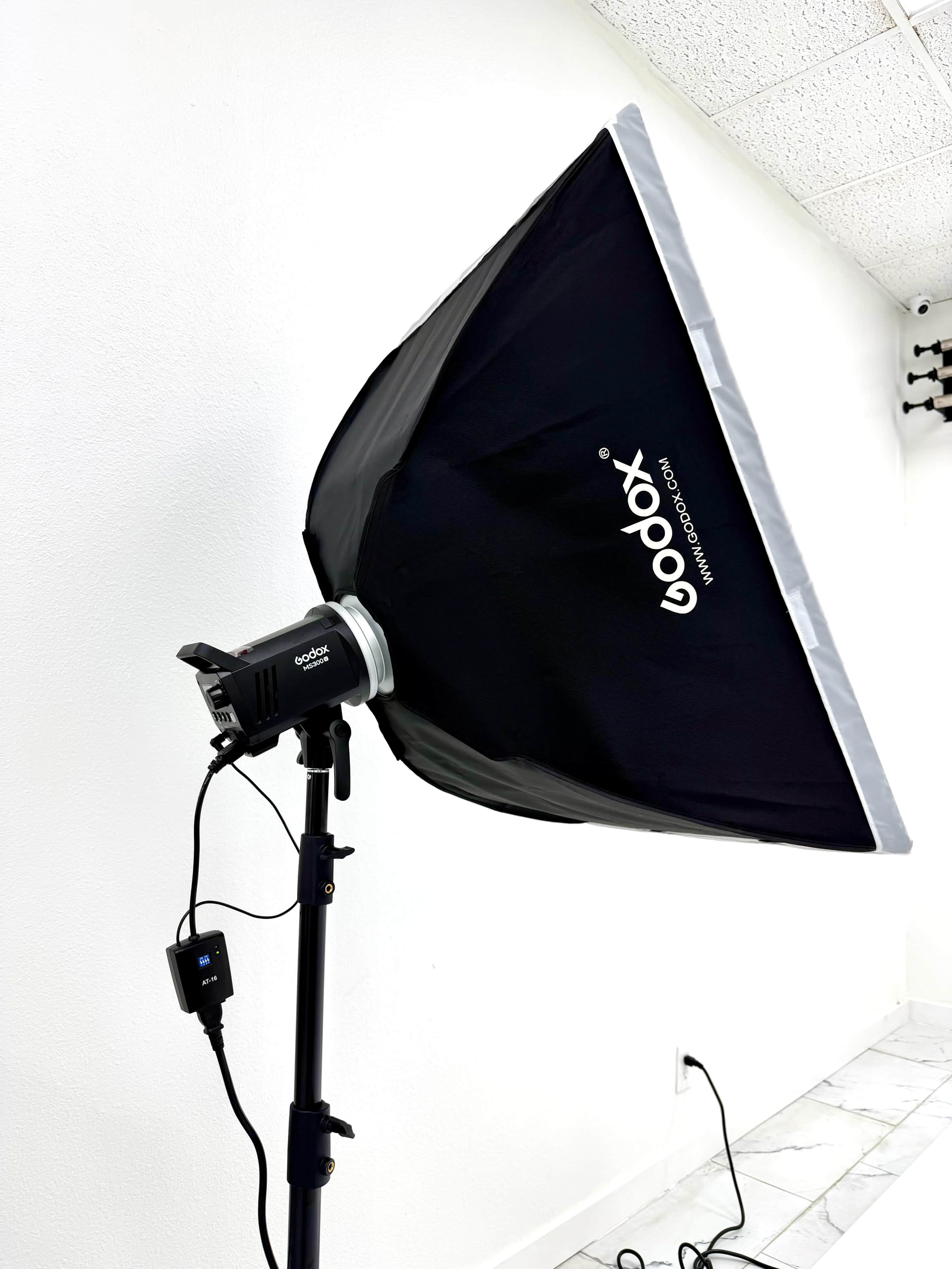 A softbox lighting fixture is mounted on a stand in a room with white walls and tiled flooring.