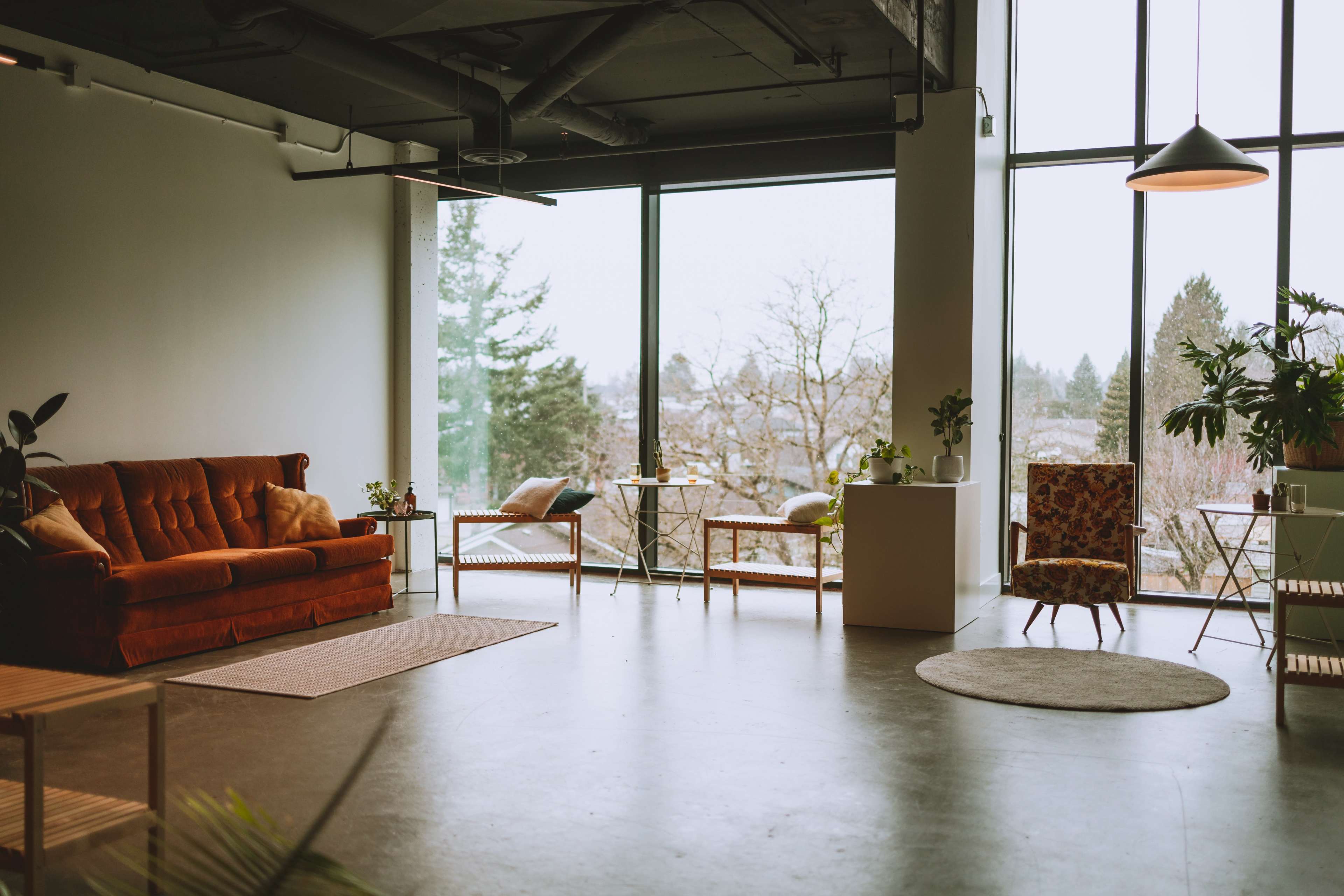 A spacious, modern living area featuring a brown sofa, a patterned chair, and large windows that overlook a tree-filled landscape.
