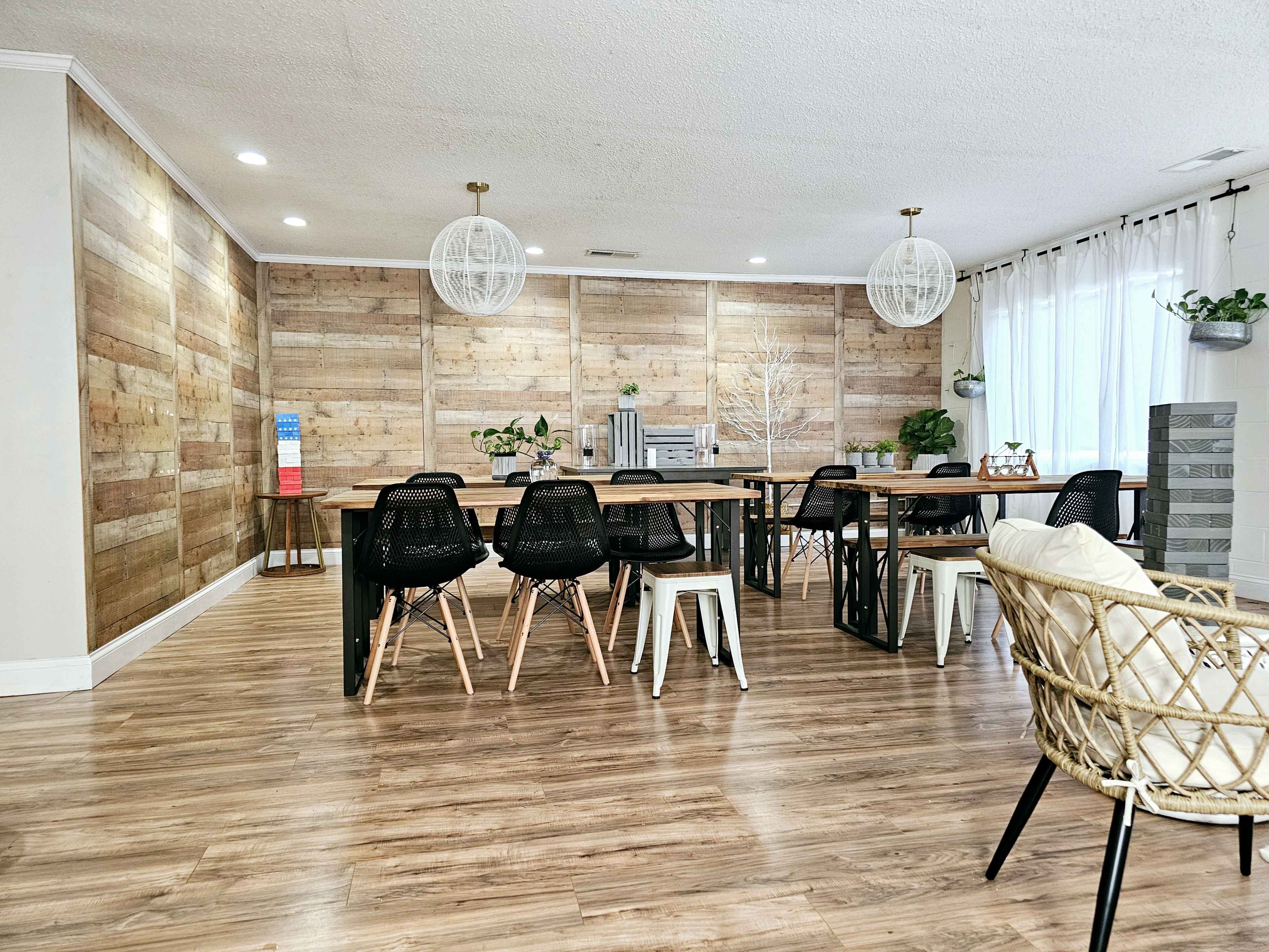 A spacious, open dining area featuring wooden walls, several tables with chairs, and pendant lighting.