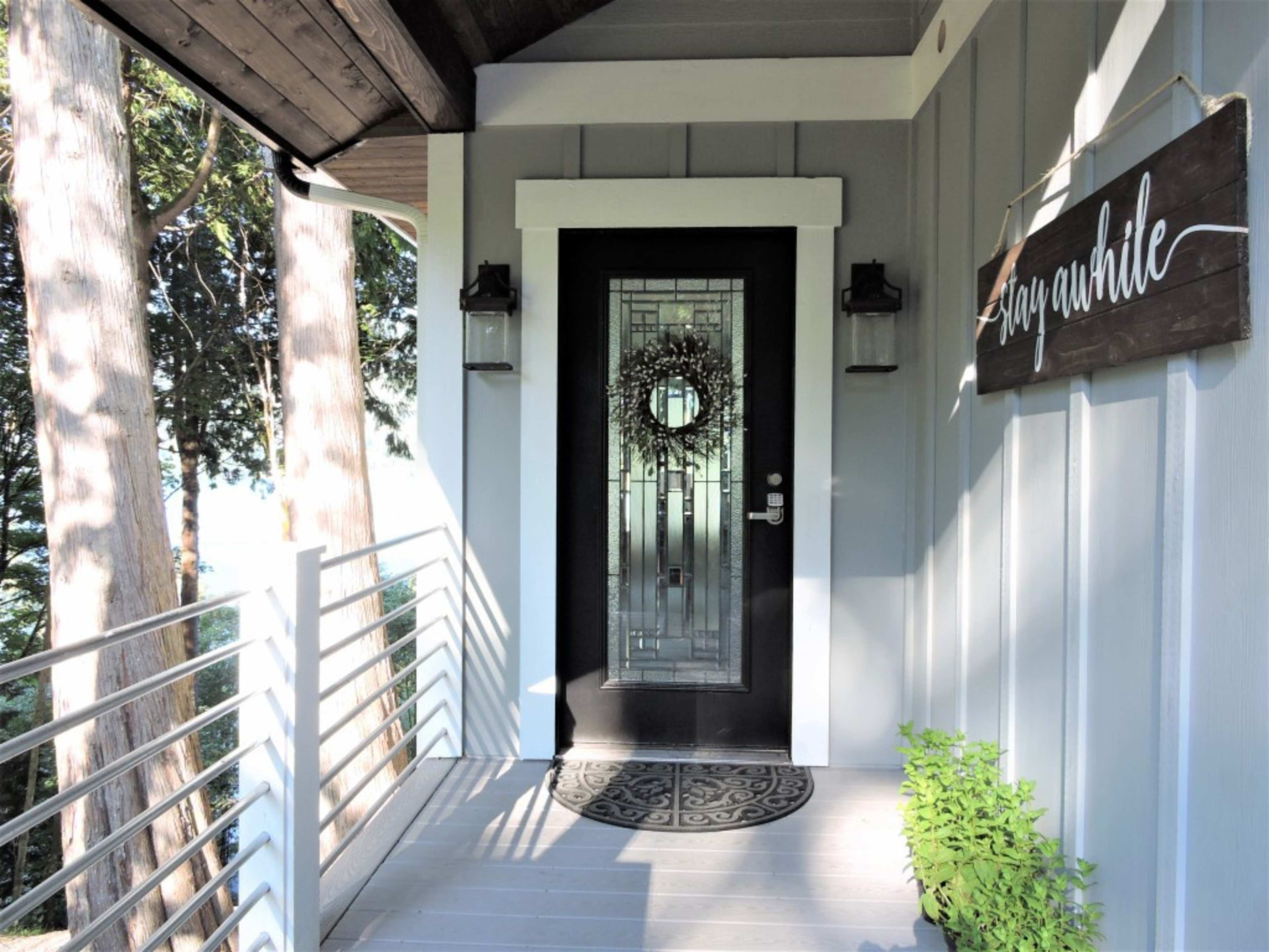 A front porch features a black door with a decorative wreath, flanked by wall sconces and a welcoming sign.