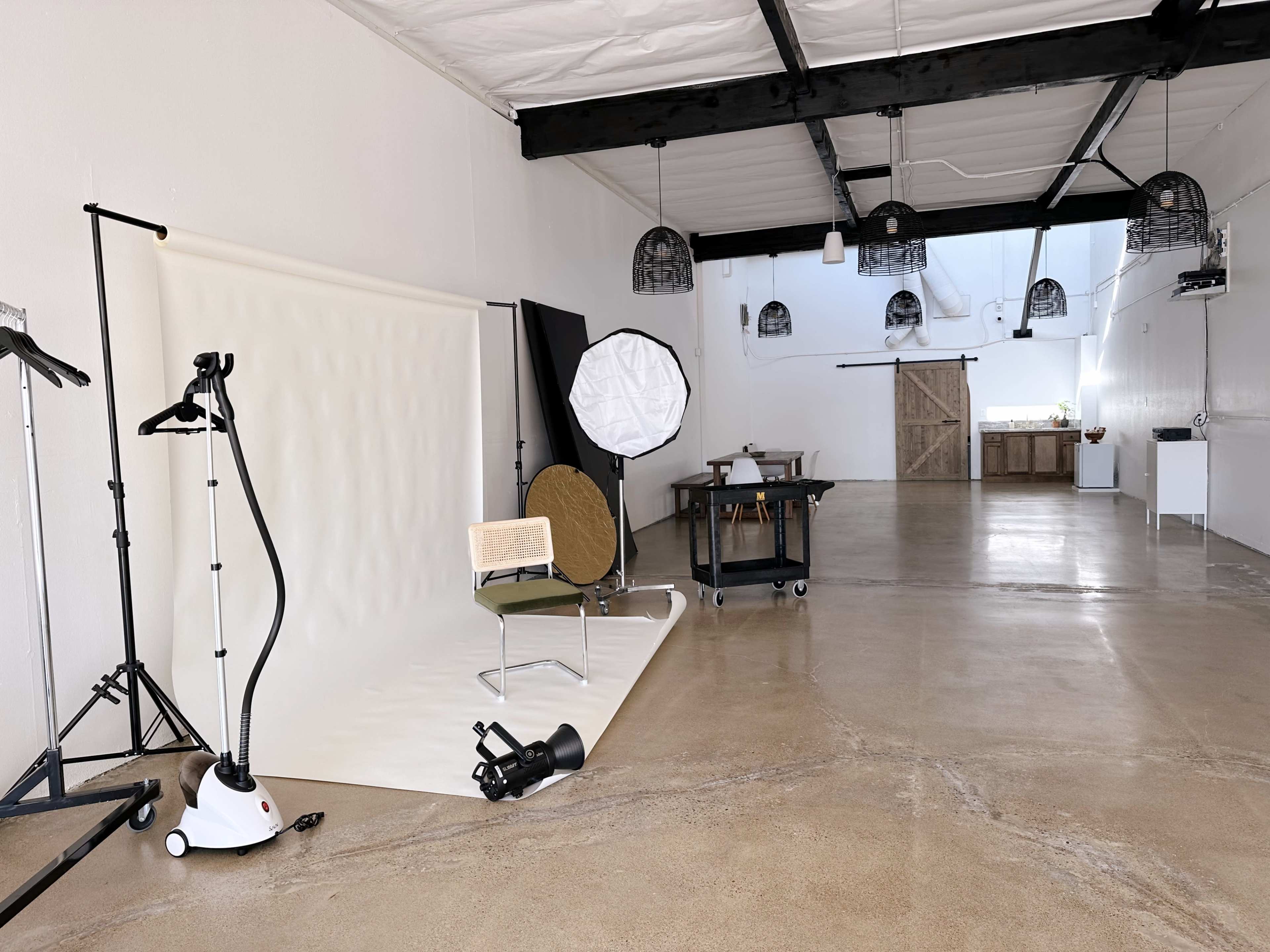 A spacious, minimally furnished studio with a photography setup, including a backdrop, lighting equipment, and a chair.