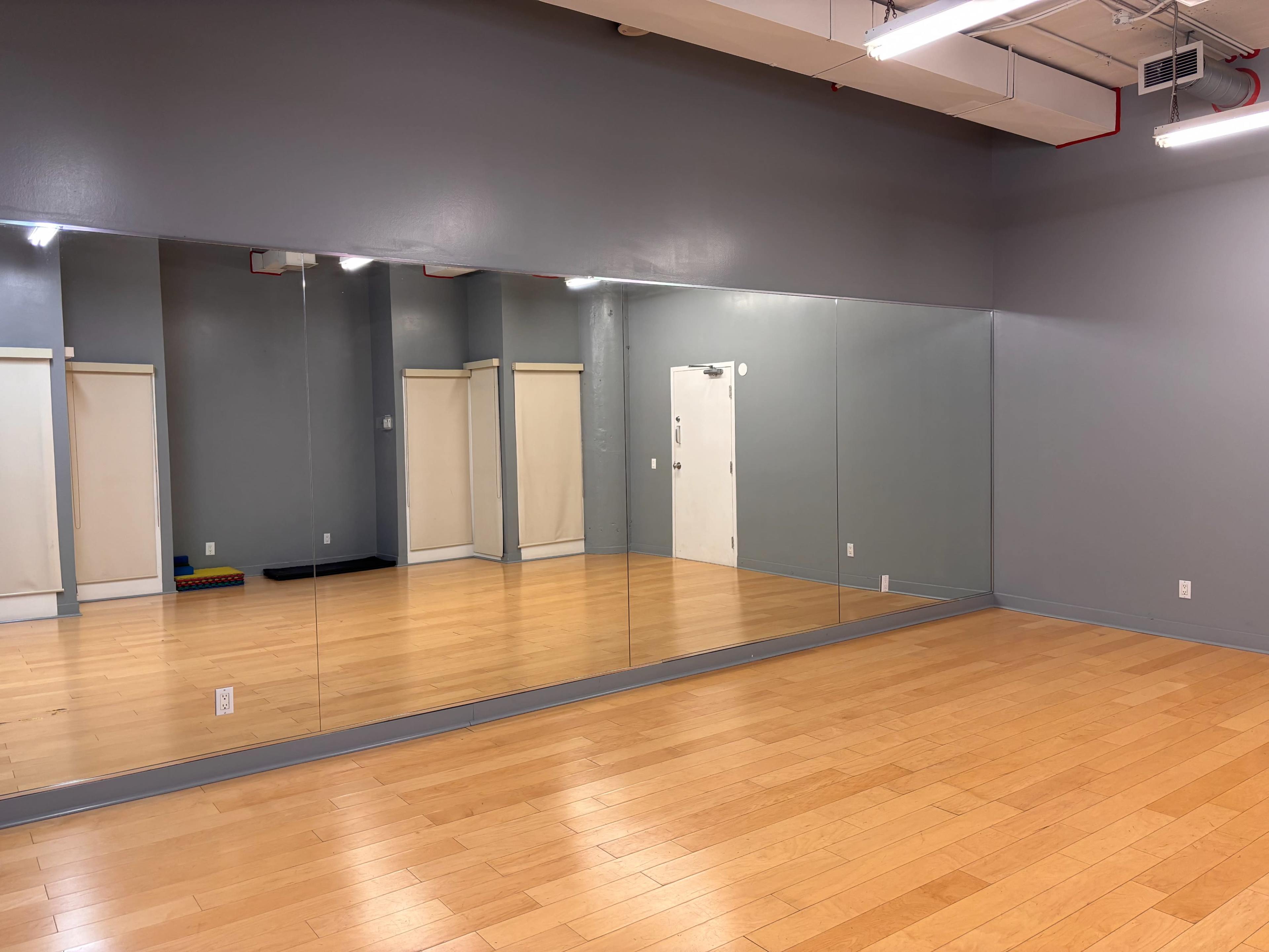 The image shows a spacious dance studio with wooden flooring and a large wall of mirrors.