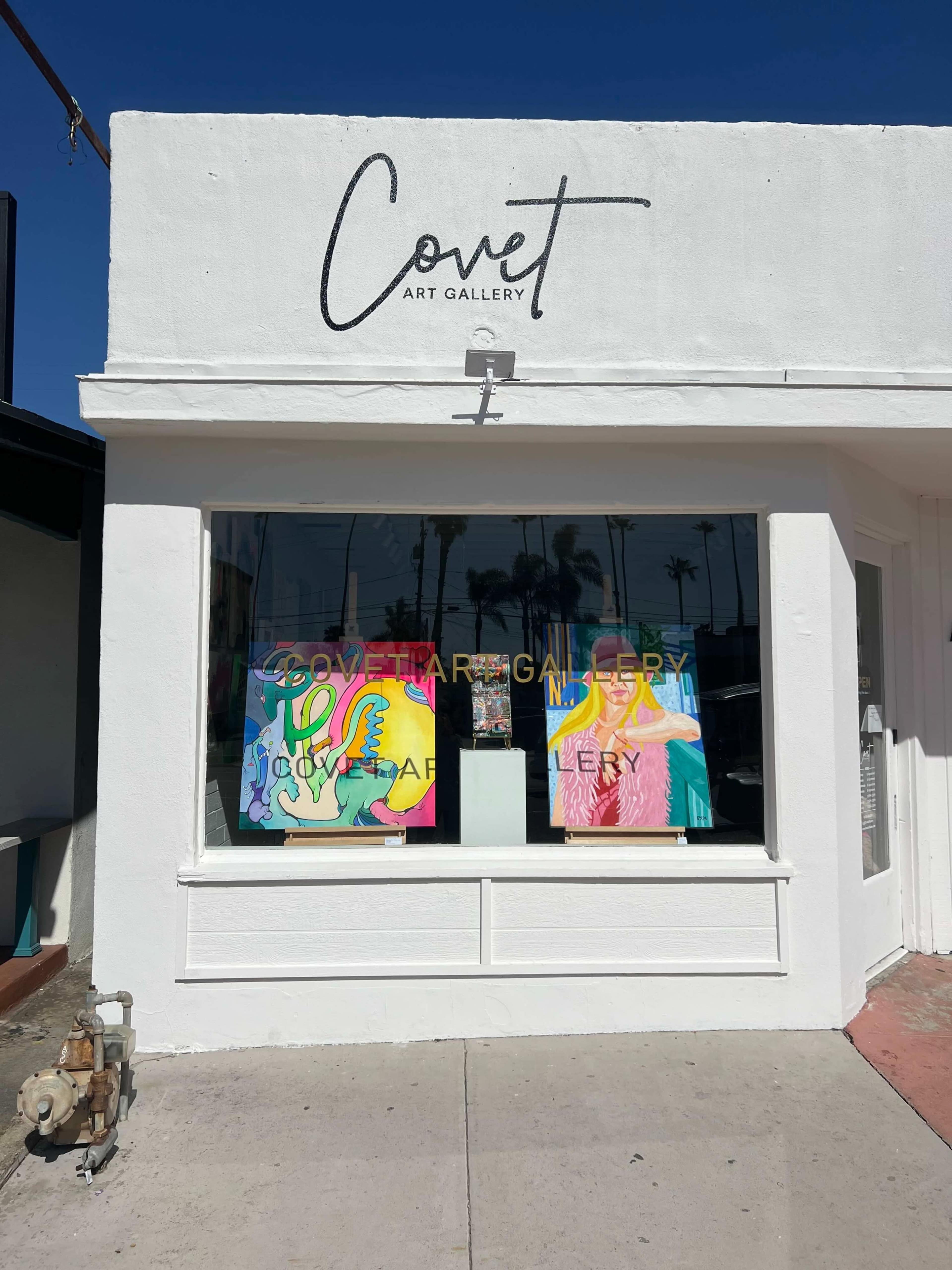 The image shows the exterior of Covet Art Gallery, featuring a colorful display in its window and a bright, clear sky above.