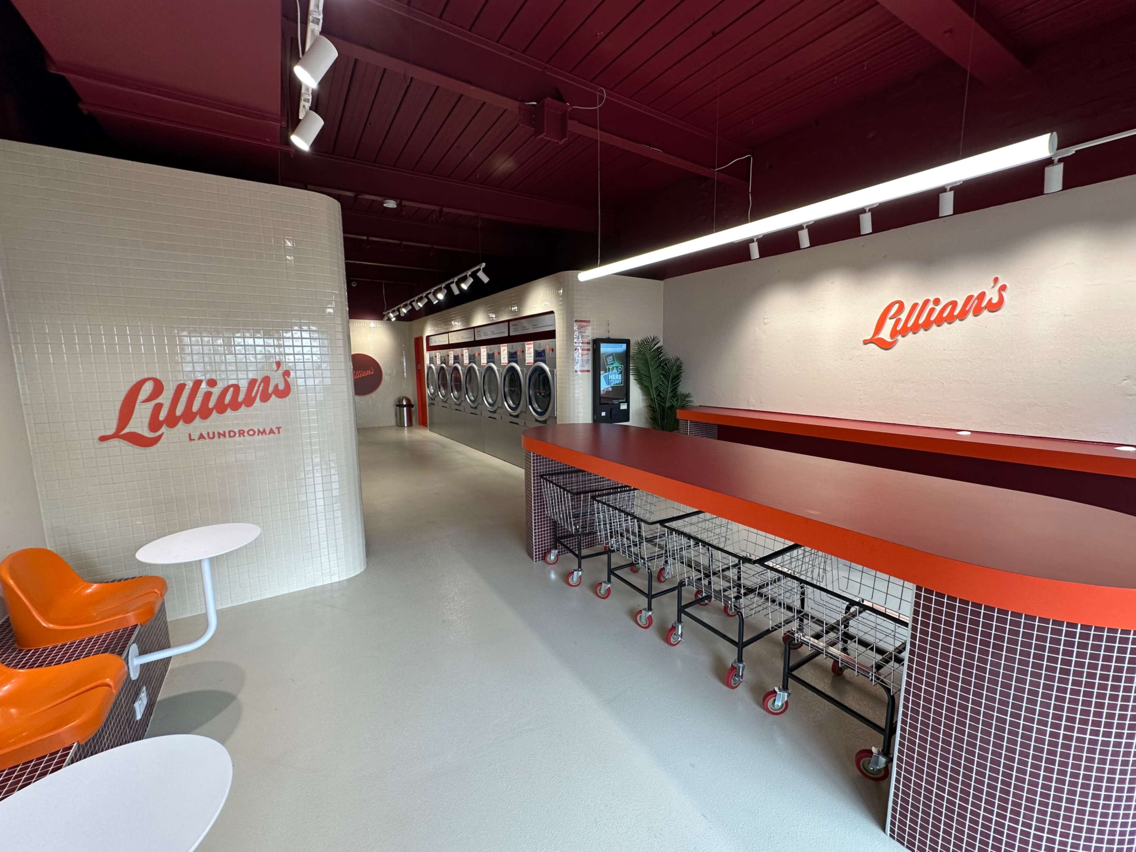 The image shows a modern laundromat interior with red accents, a long counter, and rows of washing machines.