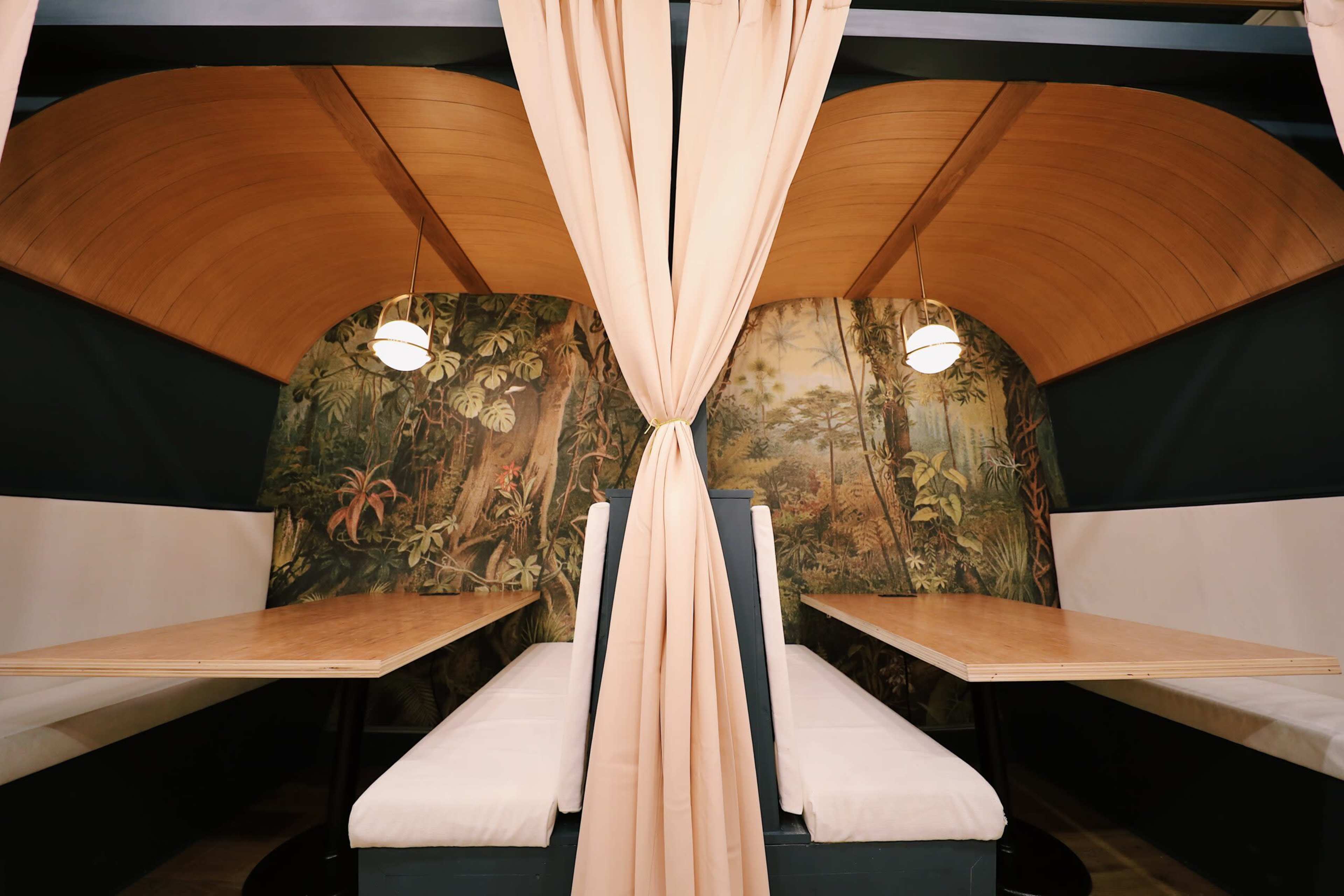 Two dining booths with wooden tables, surrounded by a tropical-themed mural and separated by soft curtains.