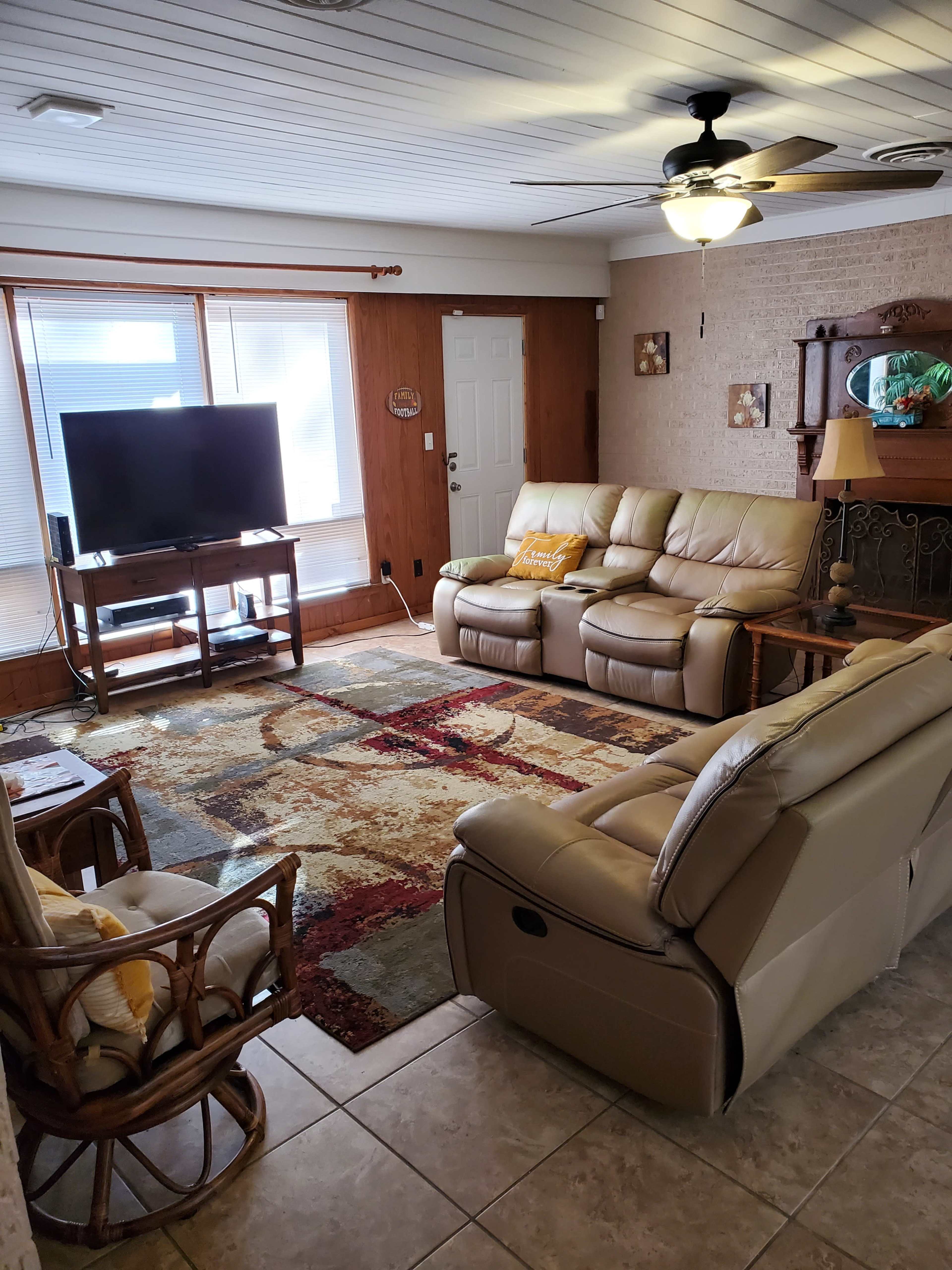 A living room with two leather sofas, a television, and a decorative area rug on tiled flooring.