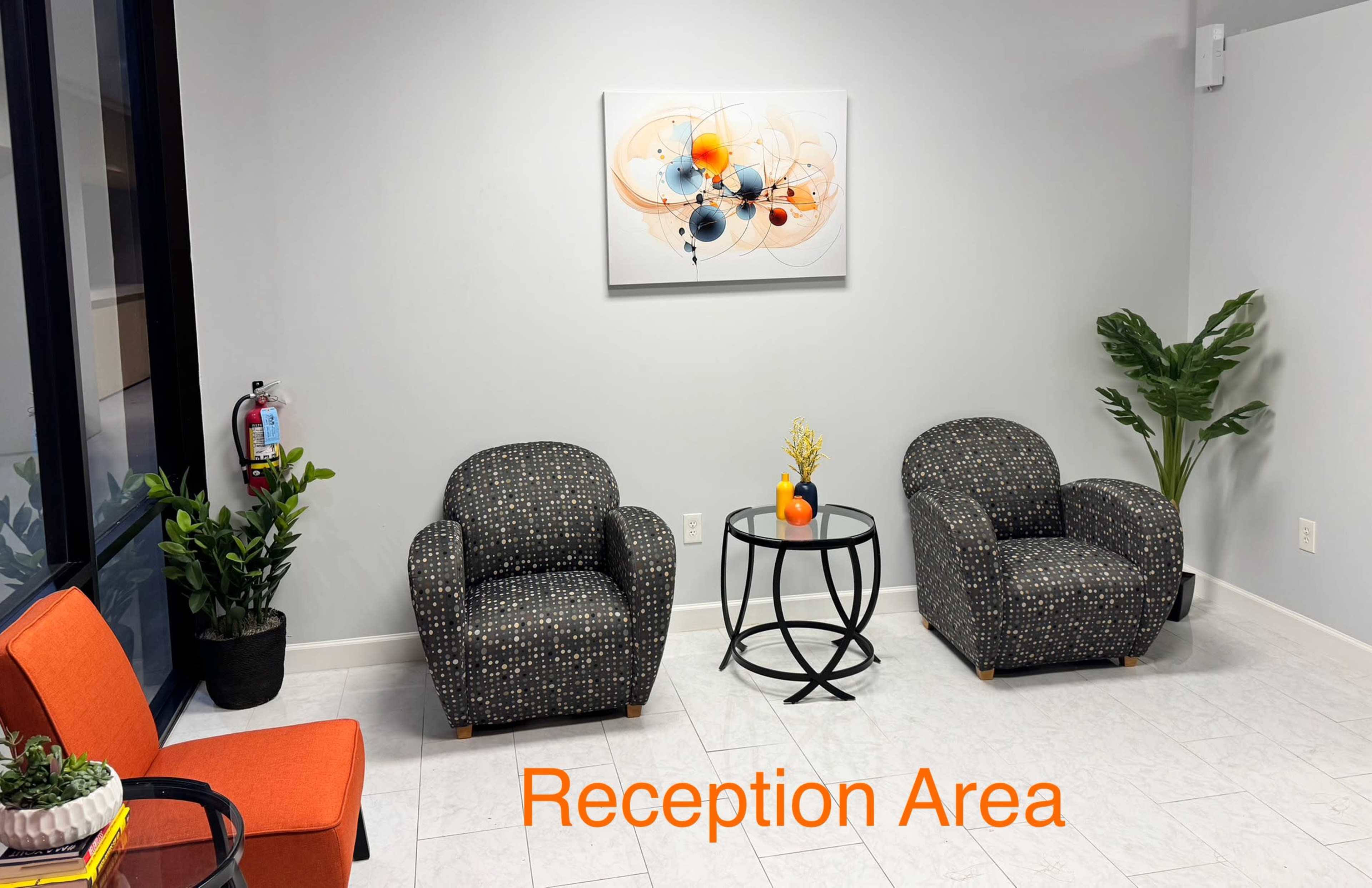 The image shows a reception area featuring two patterned armchairs, a circular black table, a small plant, and abstract artwork on the wall.