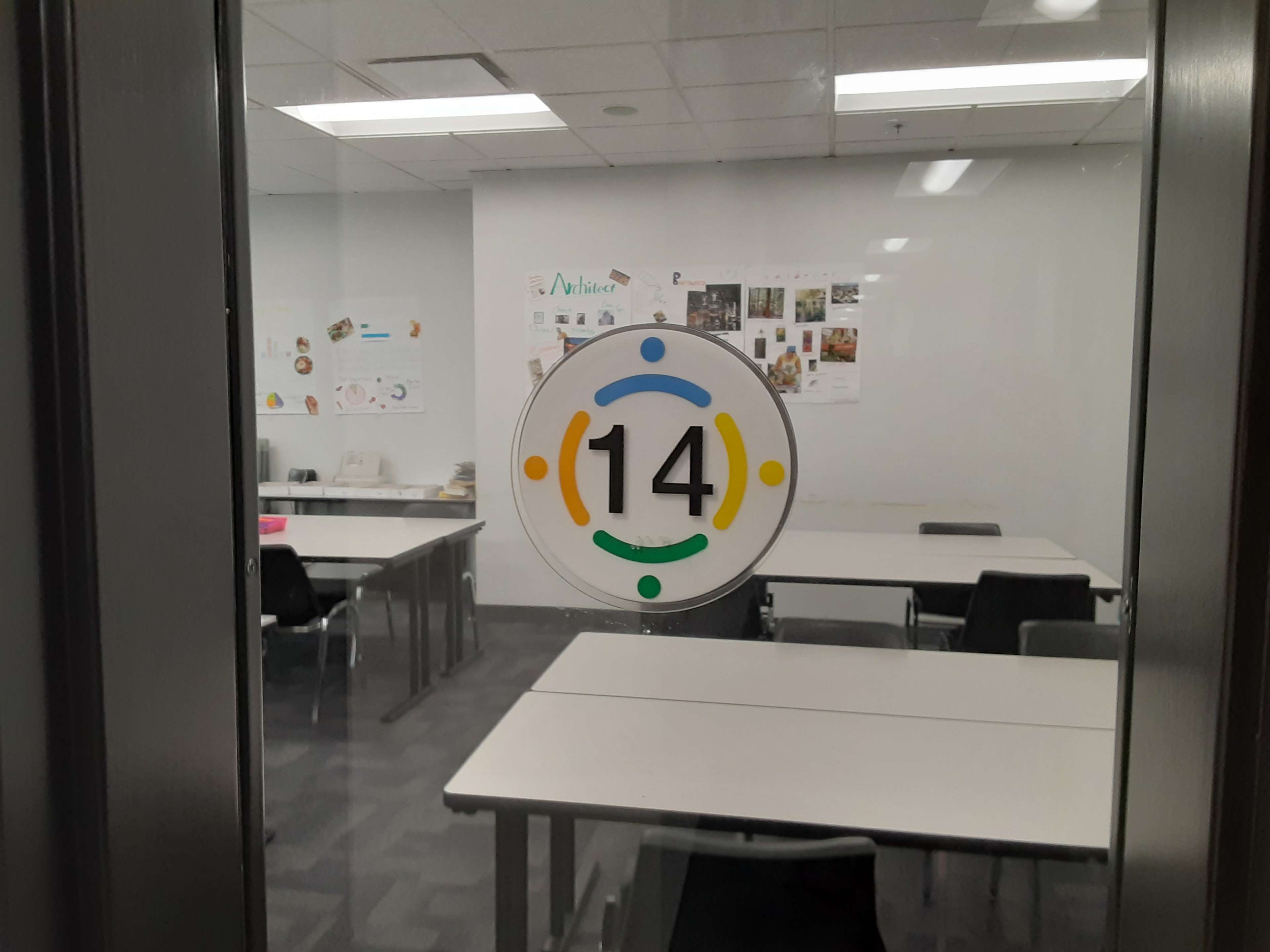 A door with a number 14 on it and a sign indicating a classroom, with tables and chairs visible through the glass.