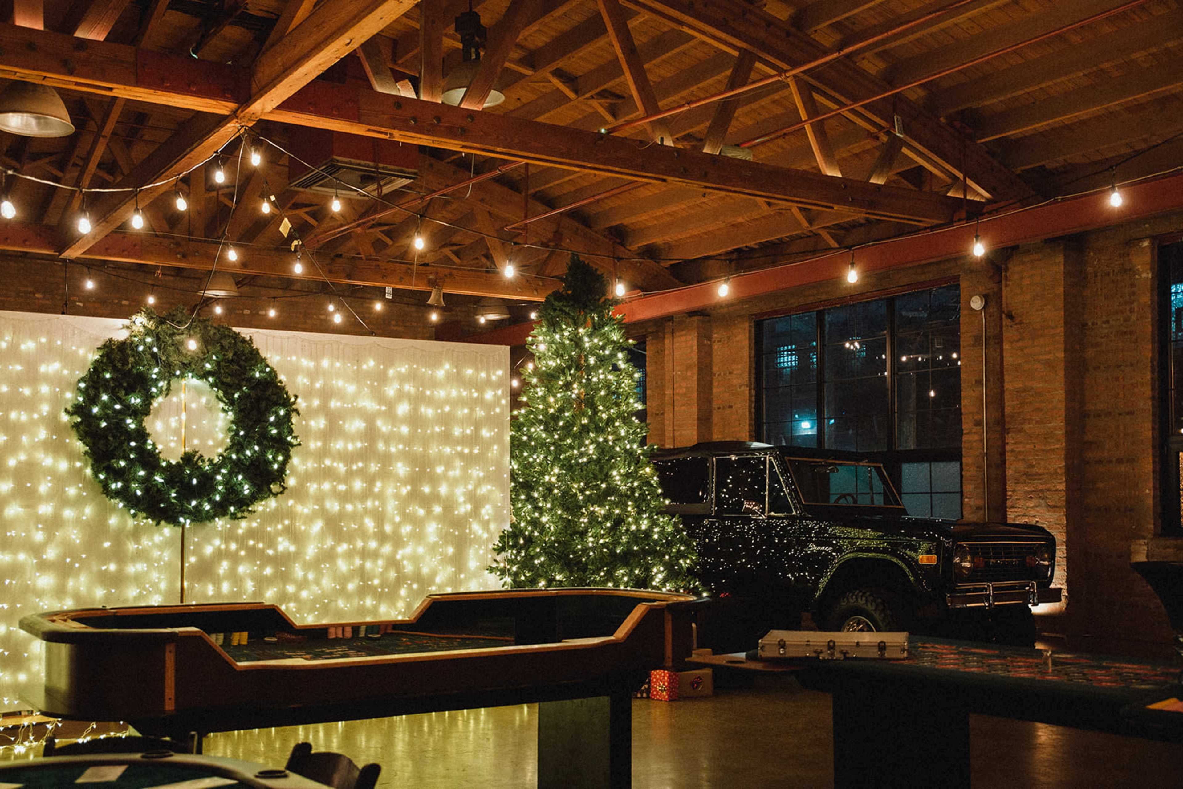 A decorated space featuring a Christmas tree, a wreath on the wall, string lights, and a vintage vehicle.