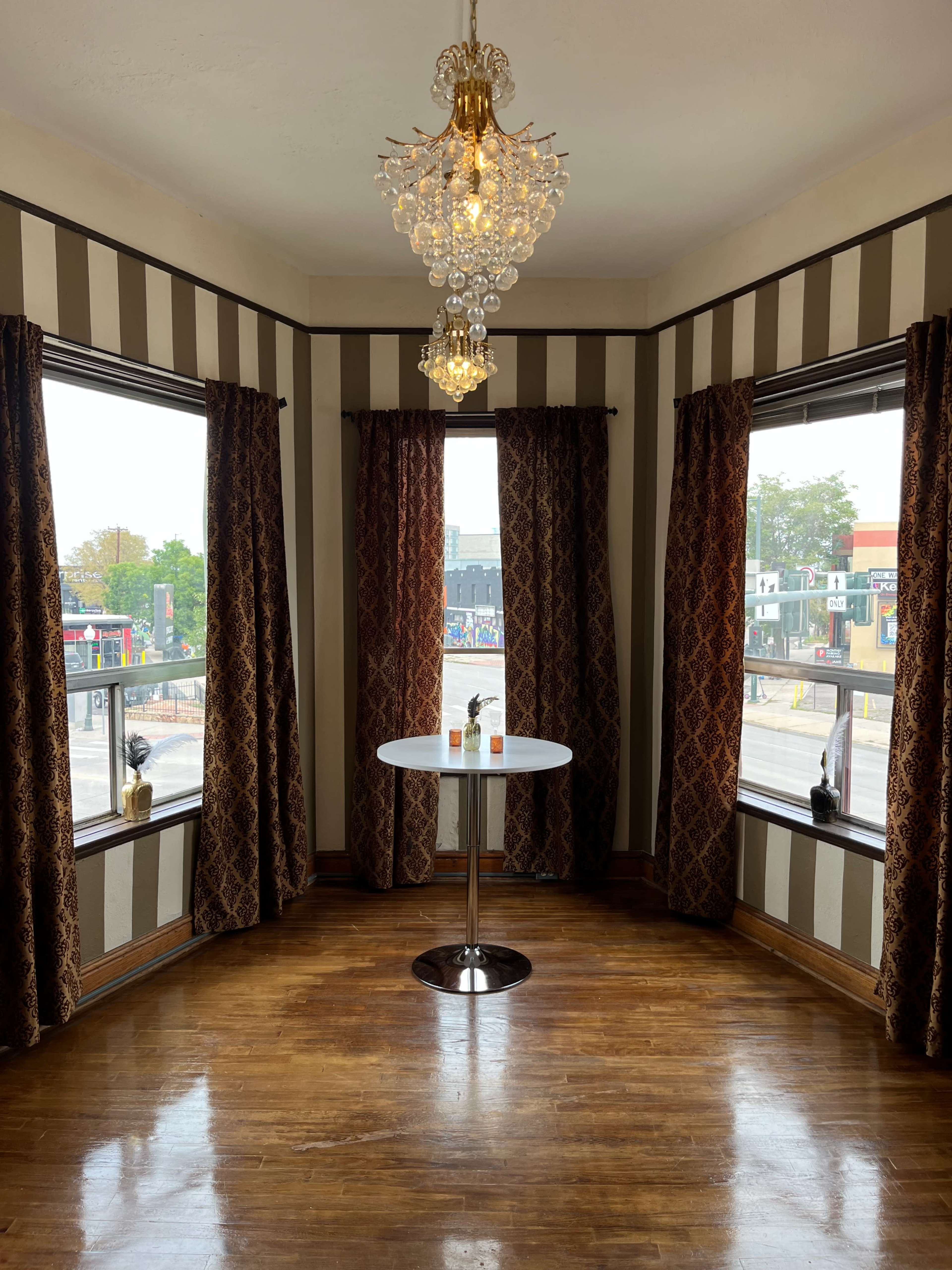 A well-lit corner of a room with two large windows, a round table in the center, and decorative curtains.
