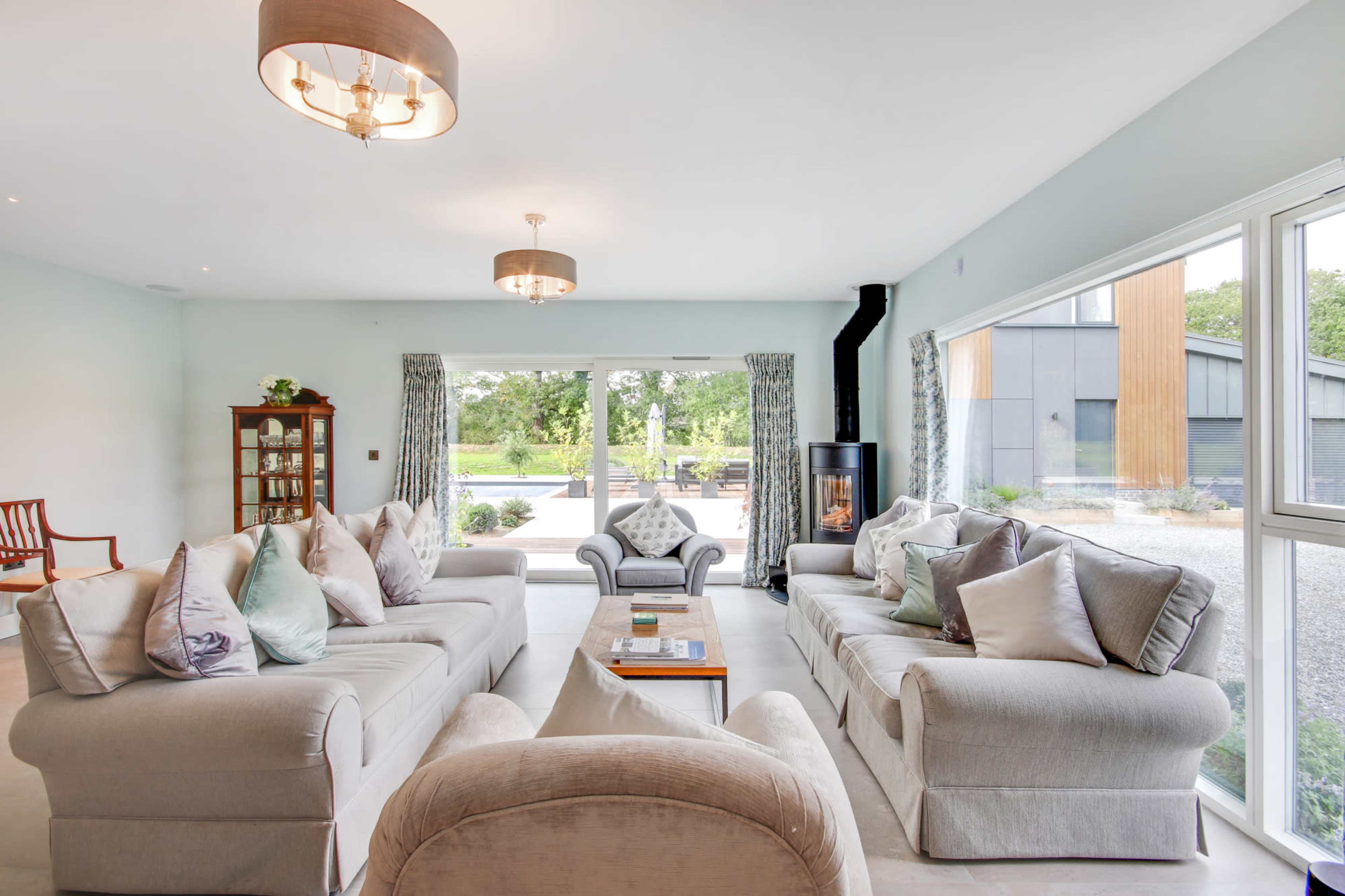 A spacious, modern living room features two large sofas, a coffee table, and a fireplace, with a view of a garden through large windows.