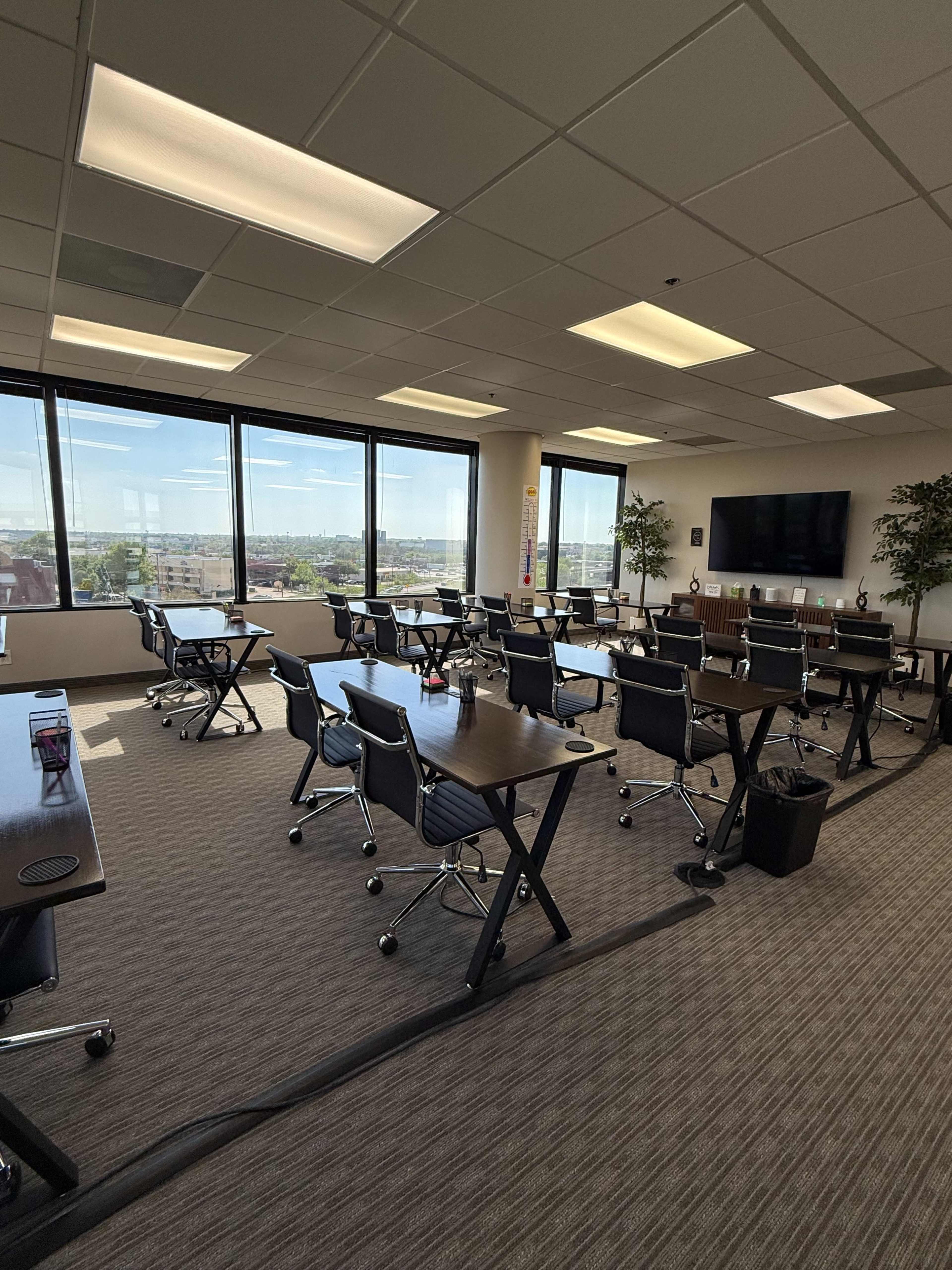 A modern conference room features several arranged tables and chairs, with large windows providing a view of the cityscape.