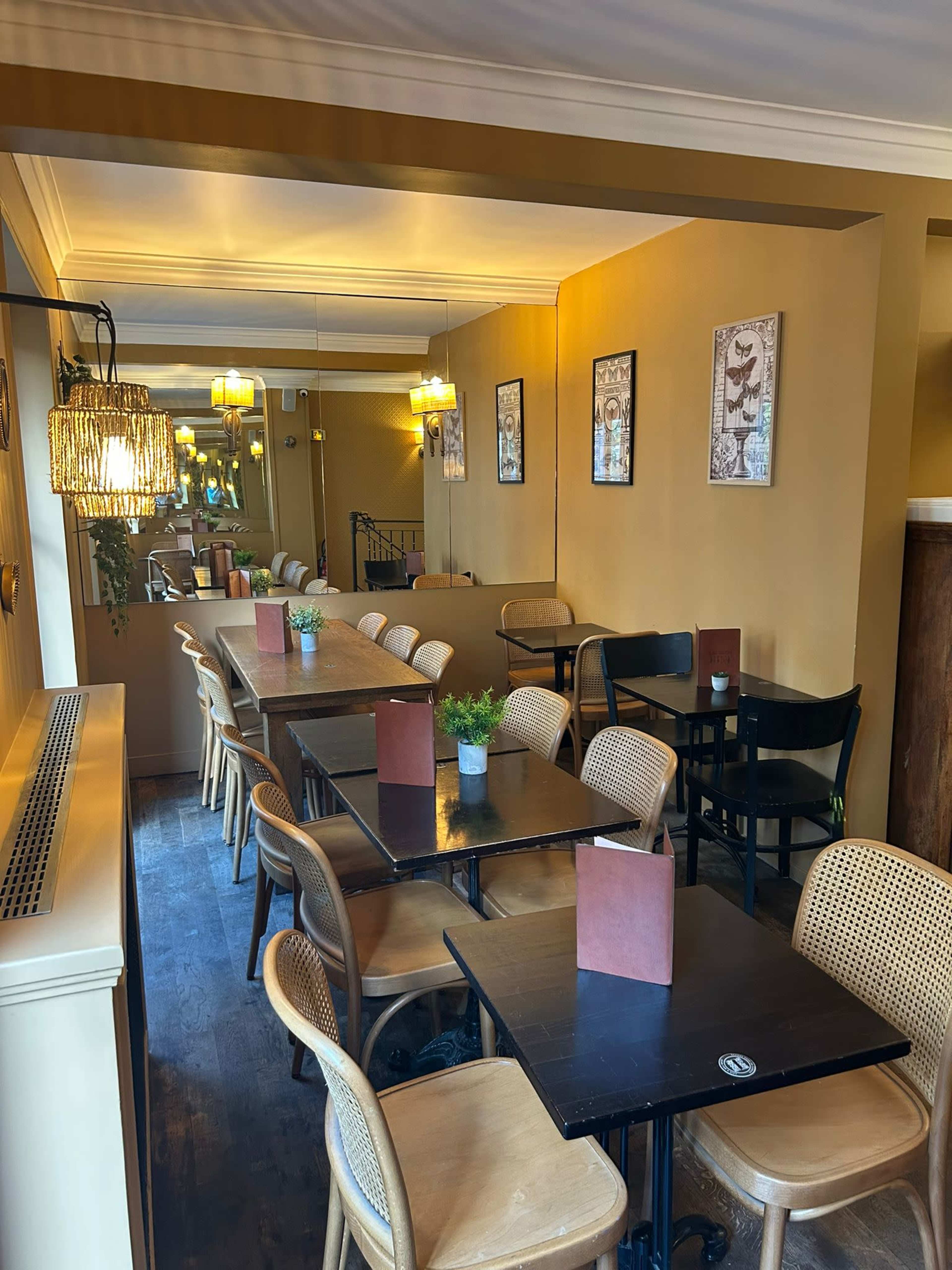 The image shows a narrow dining area with a series of tables and chairs, framed by warm-colored walls and decorative lighting.
