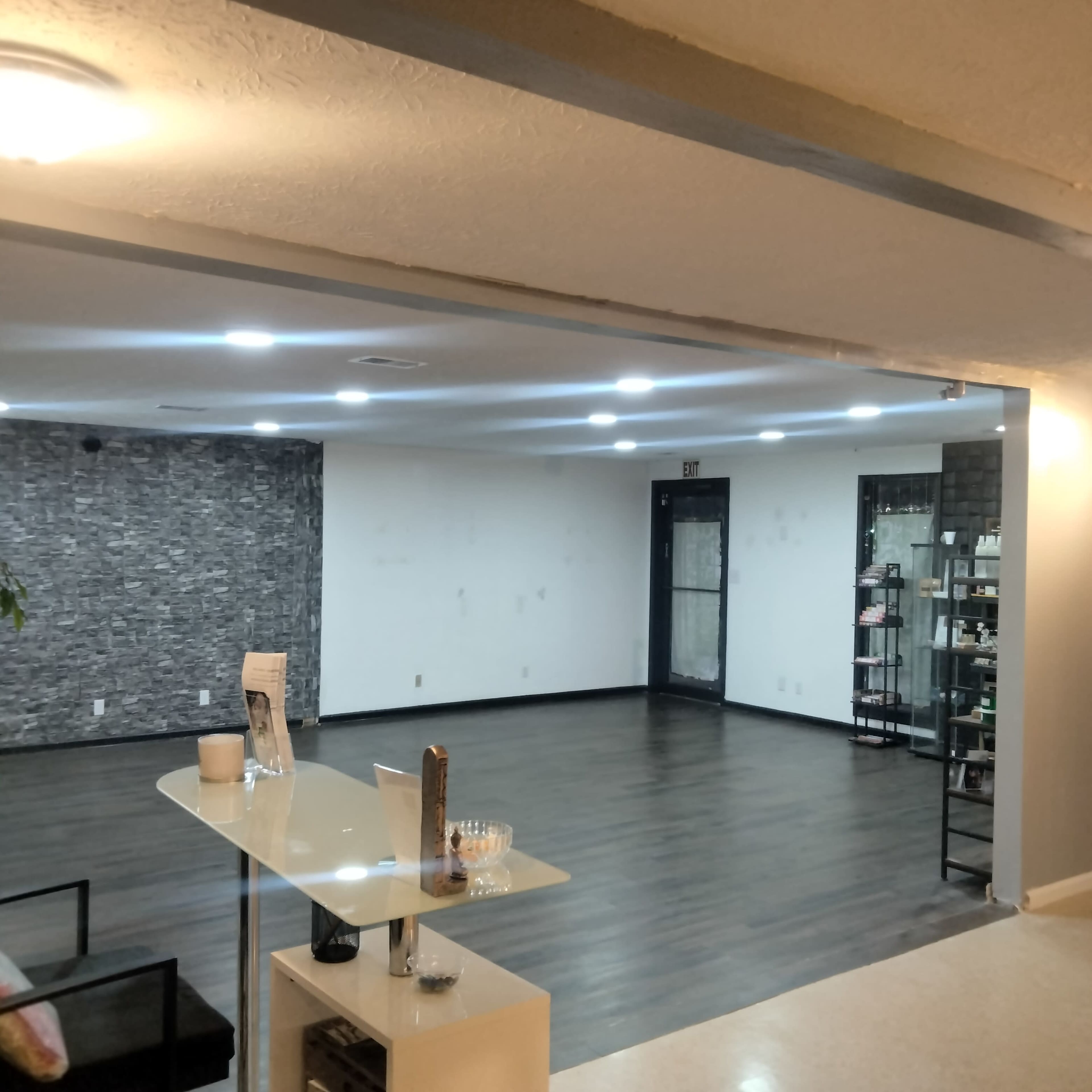 The image shows a spacious, minimalistic interior with a reception area, an empty floor, and a display shelving unit along one wall.