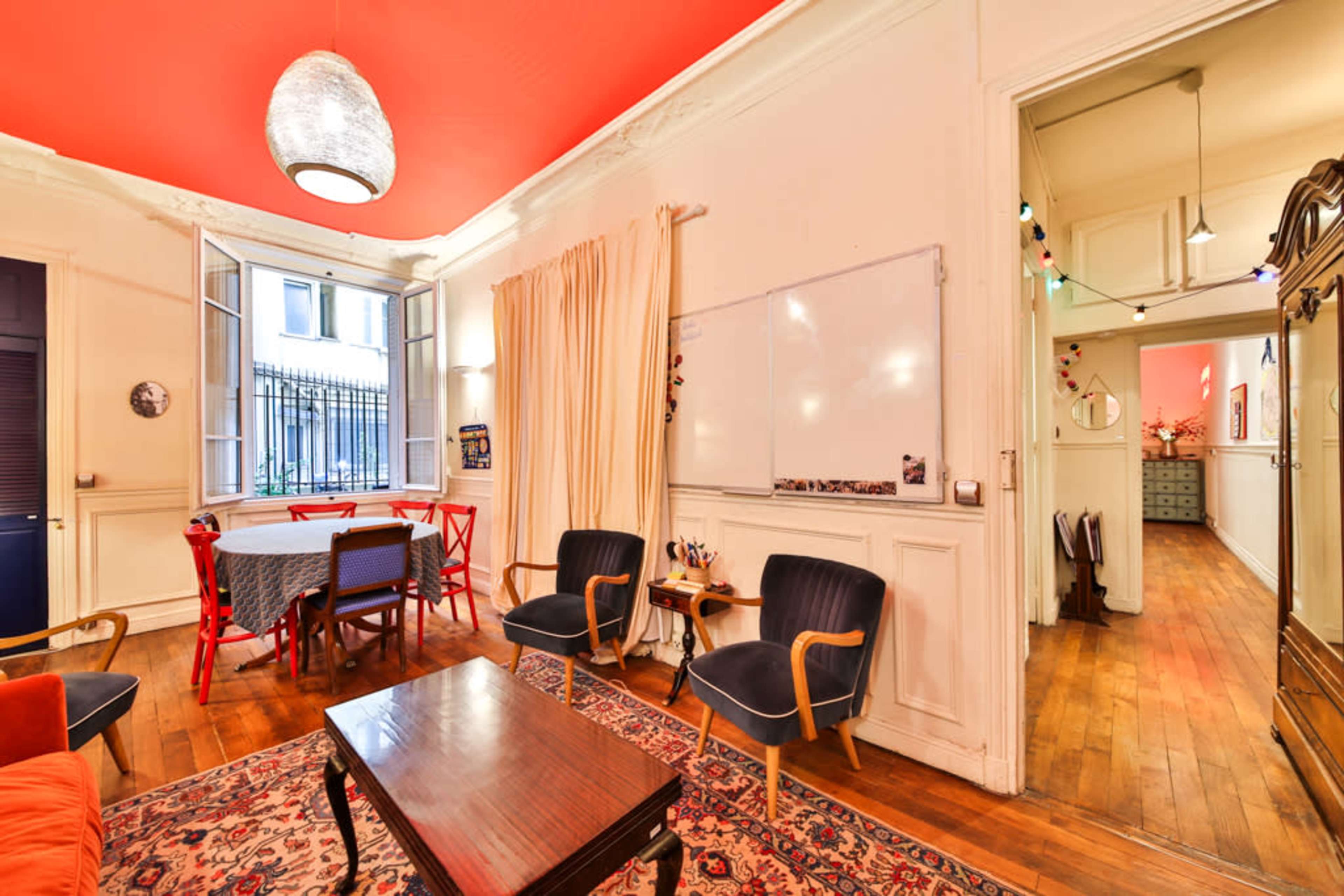 The image shows a room with a red ceiling, hardwood floors, a dining table with red chairs, two armchairs, and a whiteboard on the wall.