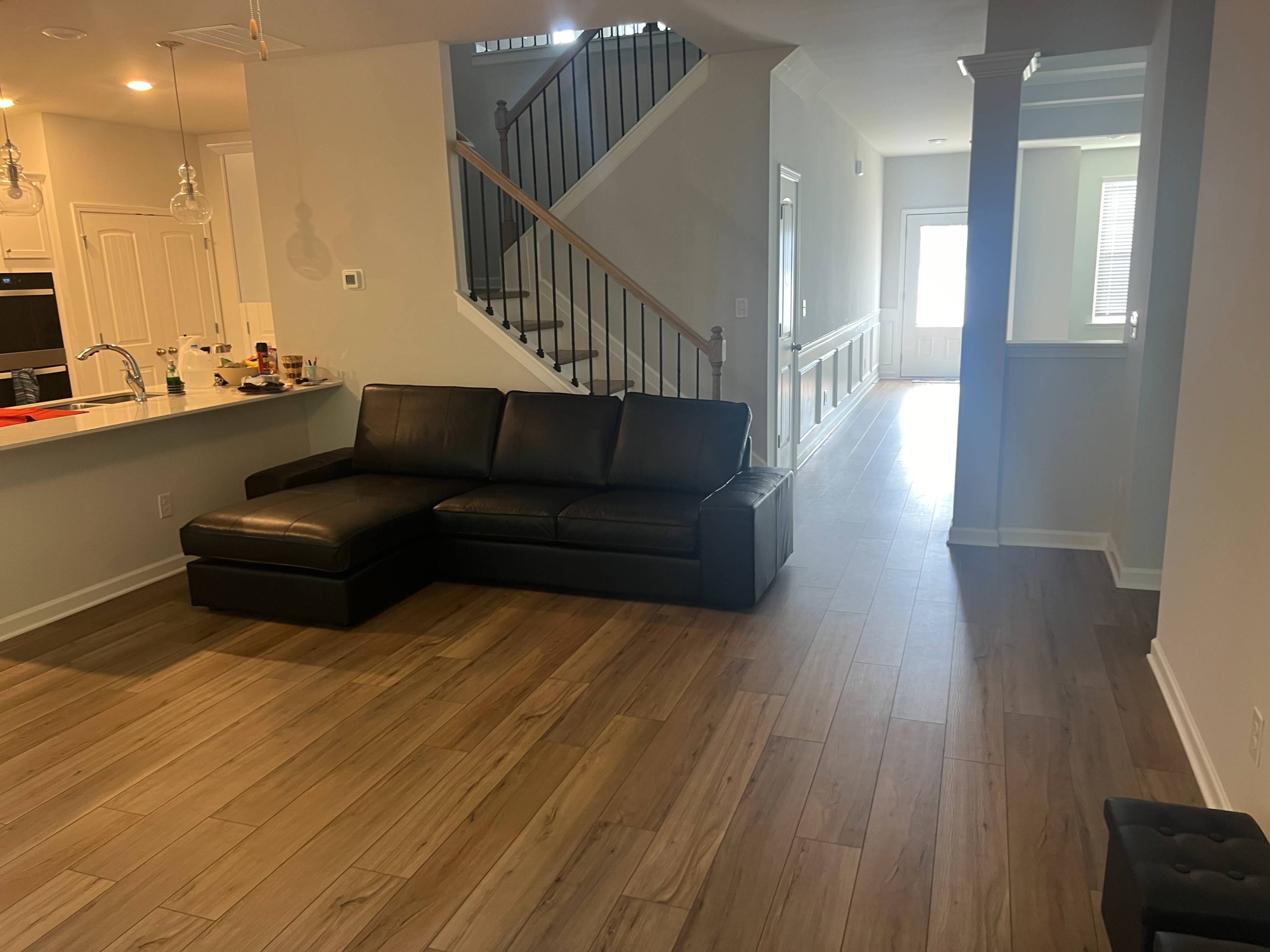 A modern living space with a dark sectional sofa, a wooden floor, and a staircase leading to an upper level.