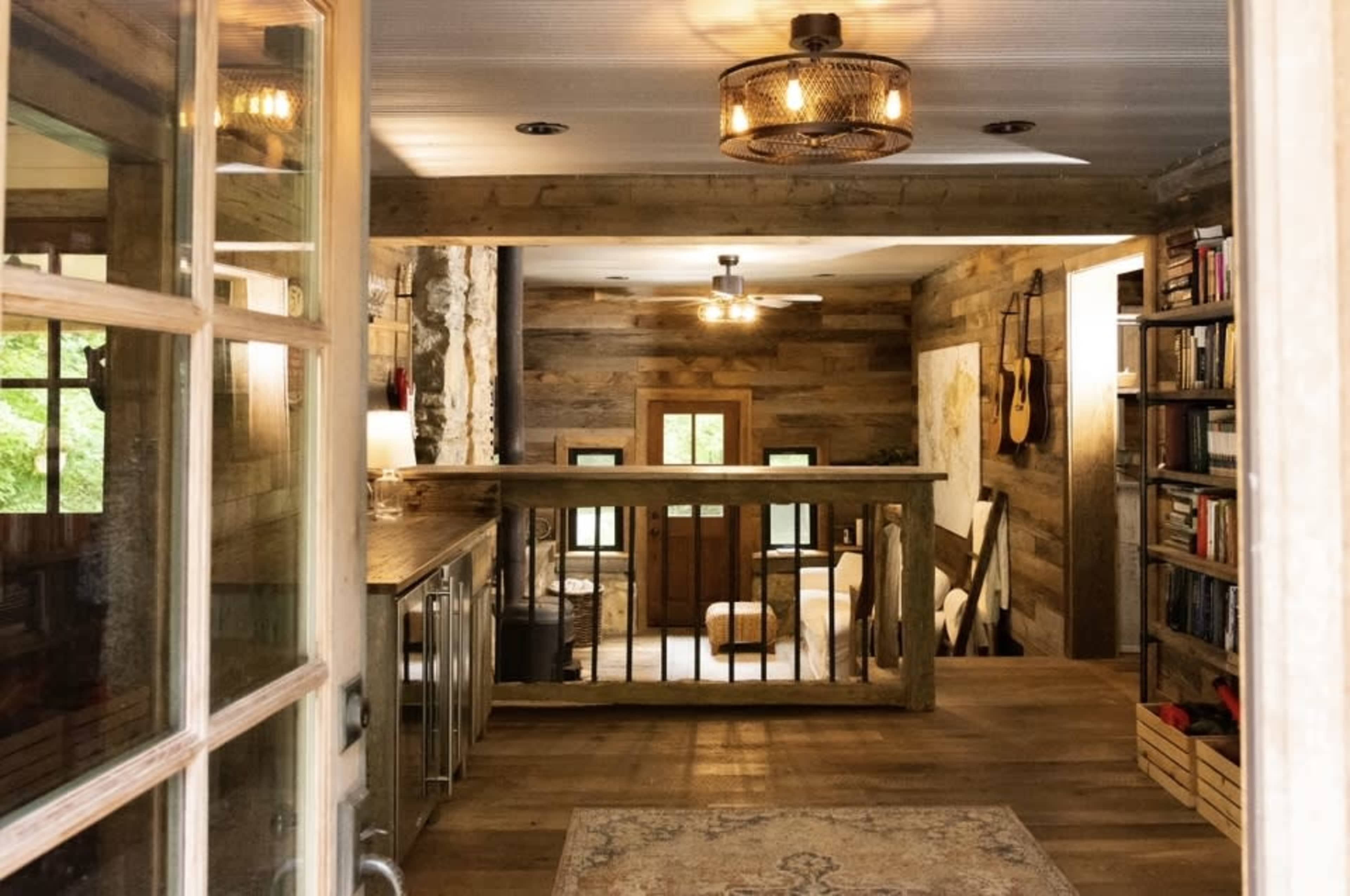 A rustic interior space featuring wooden walls, a balcony overlooking a cozy living area with bookshelves and guitars on display.