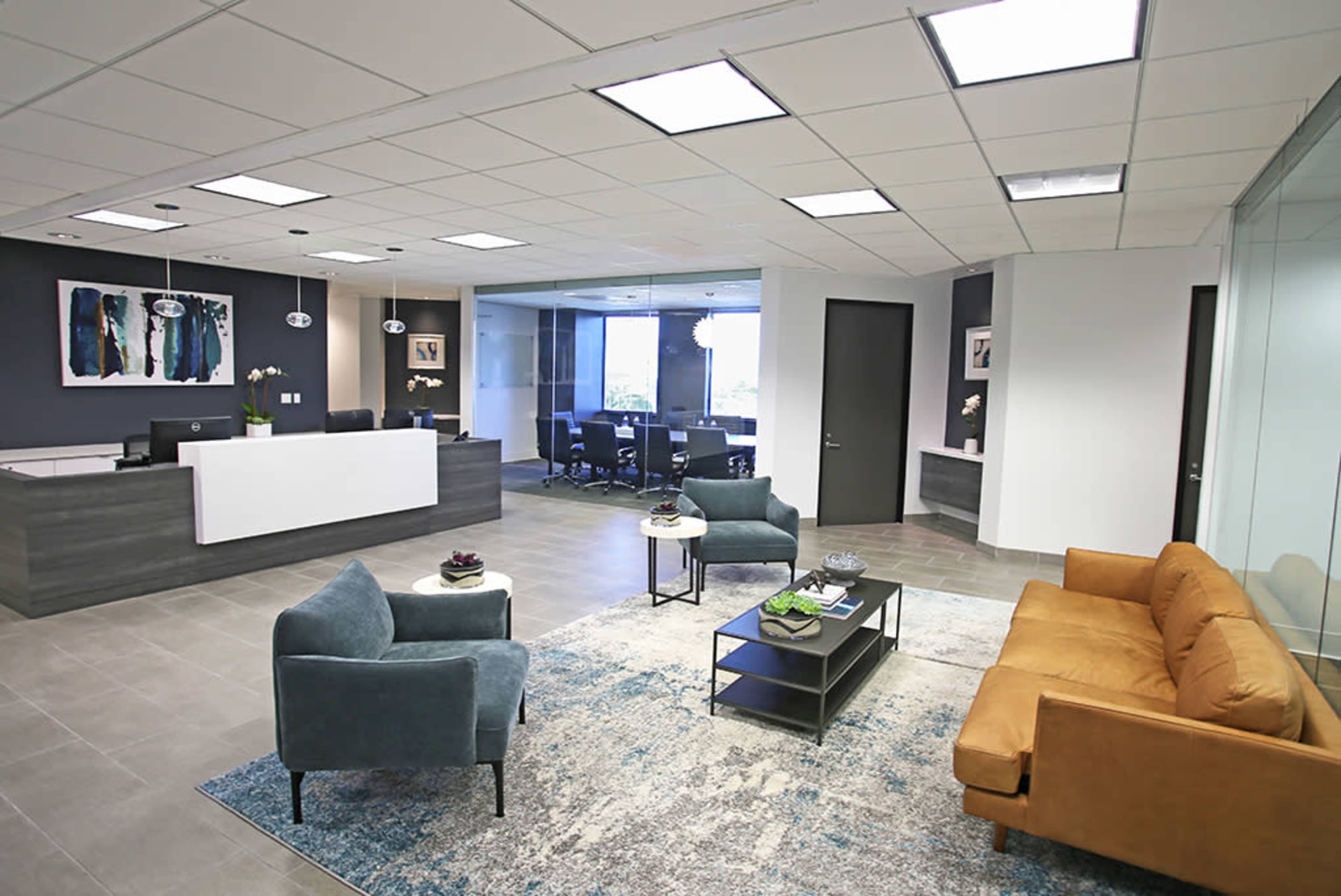 A modern office reception area featuring seating, a coffee table, and a conference room visible through glass walls.