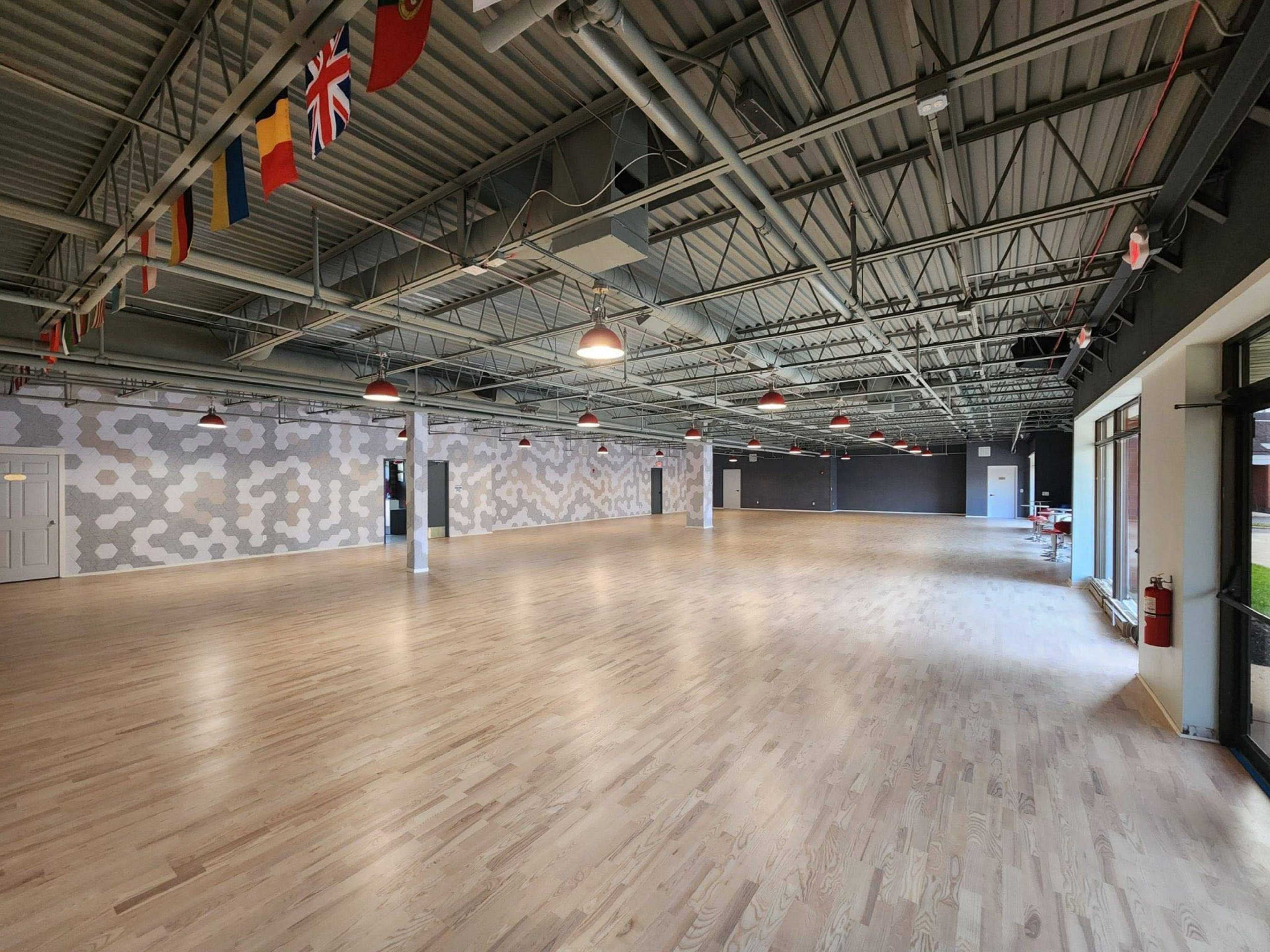 The image shows a spacious interior with wooden flooring, high ceilings, and flags hanging from above.