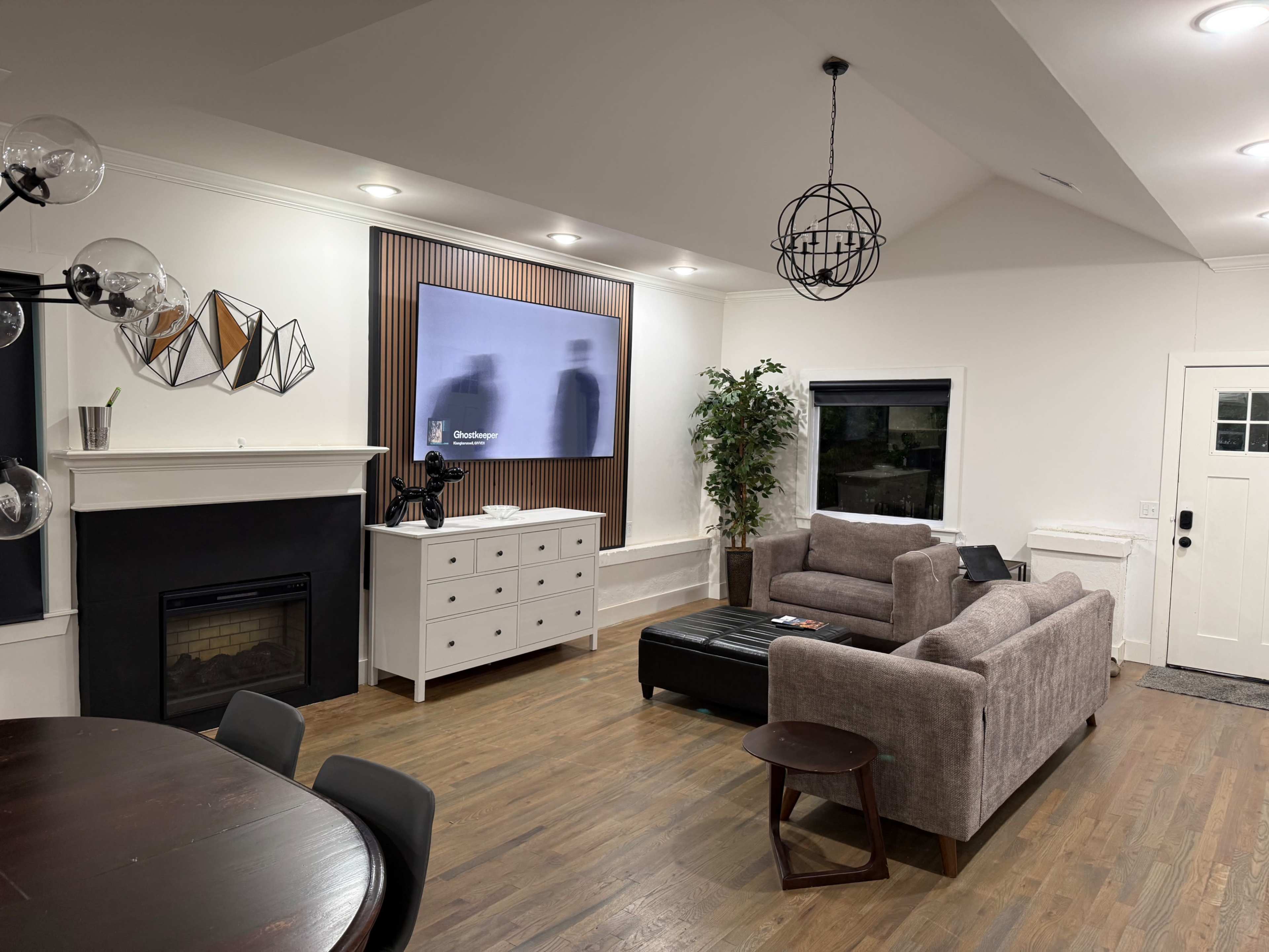 The image shows a modern living room with a fireplace, a wall-mounted TV, a sectional sofa, and a dining table.
