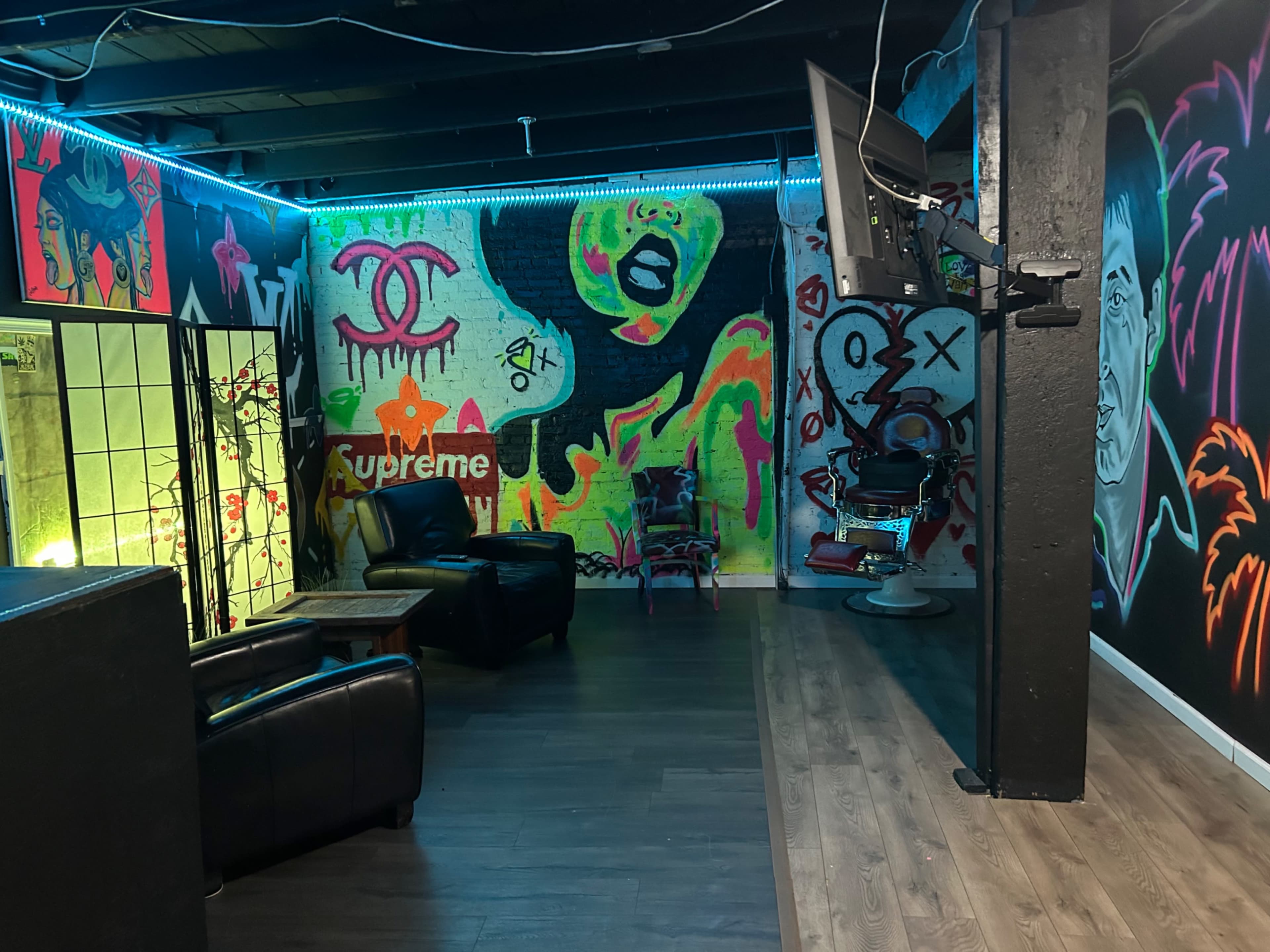 The image shows a modern lounge area with graffiti-covered walls, a television mounted on a pillar, and leather seating.
