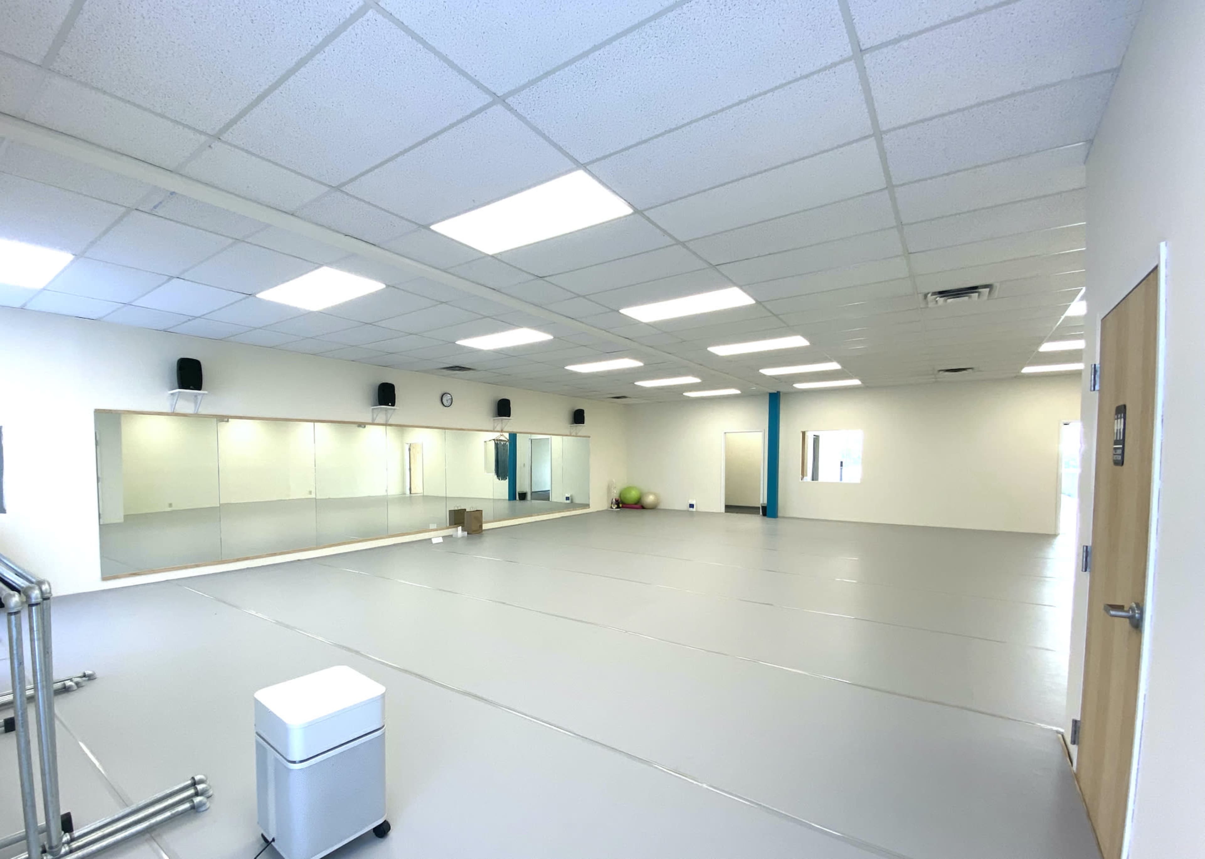 A spacious, empty room with mirrored walls, gray flooring, and minimal furnishings.