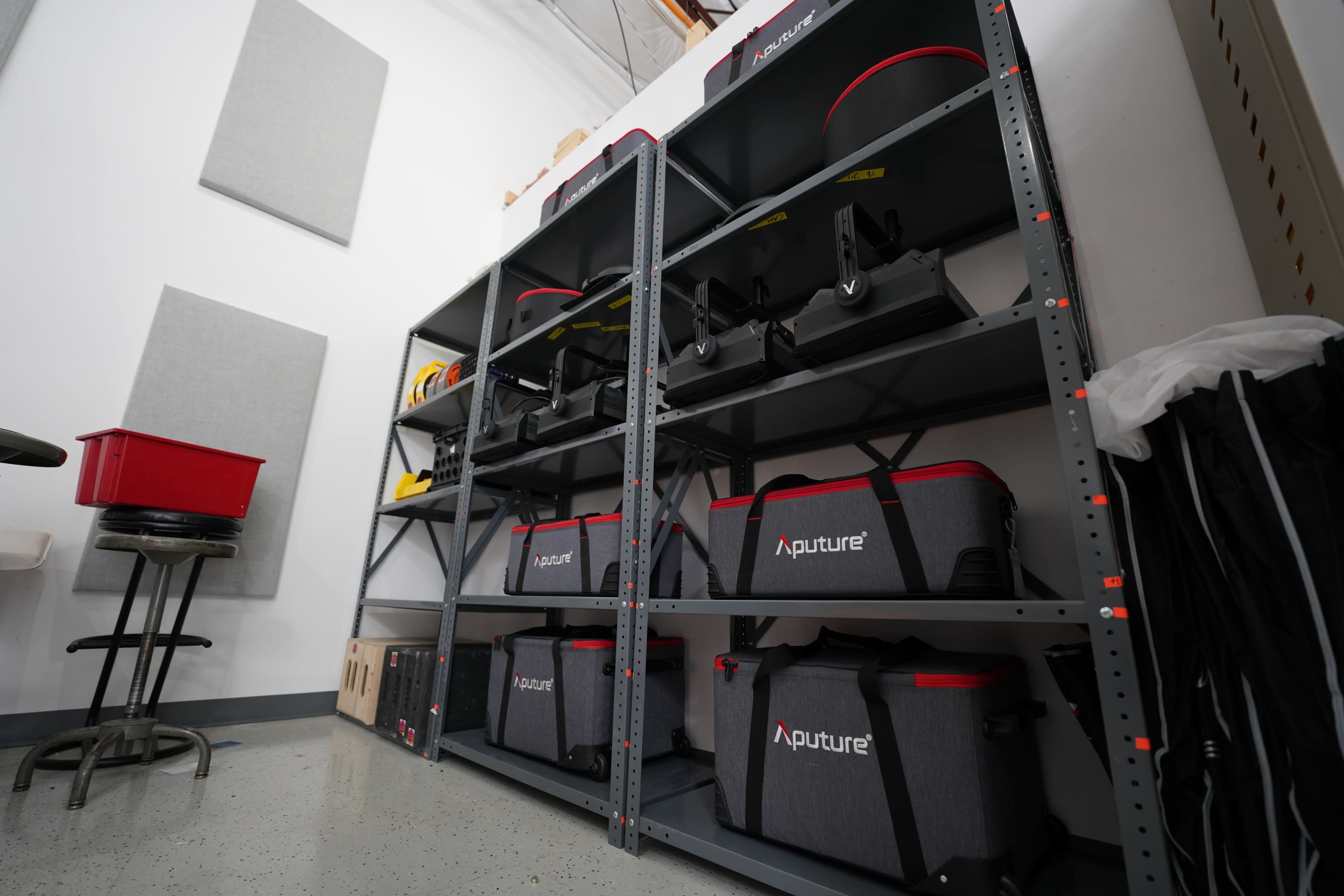 The image shows a metal shelving unit filled with gray storage bags labeled “Aputure” in a room with minimalist decor.