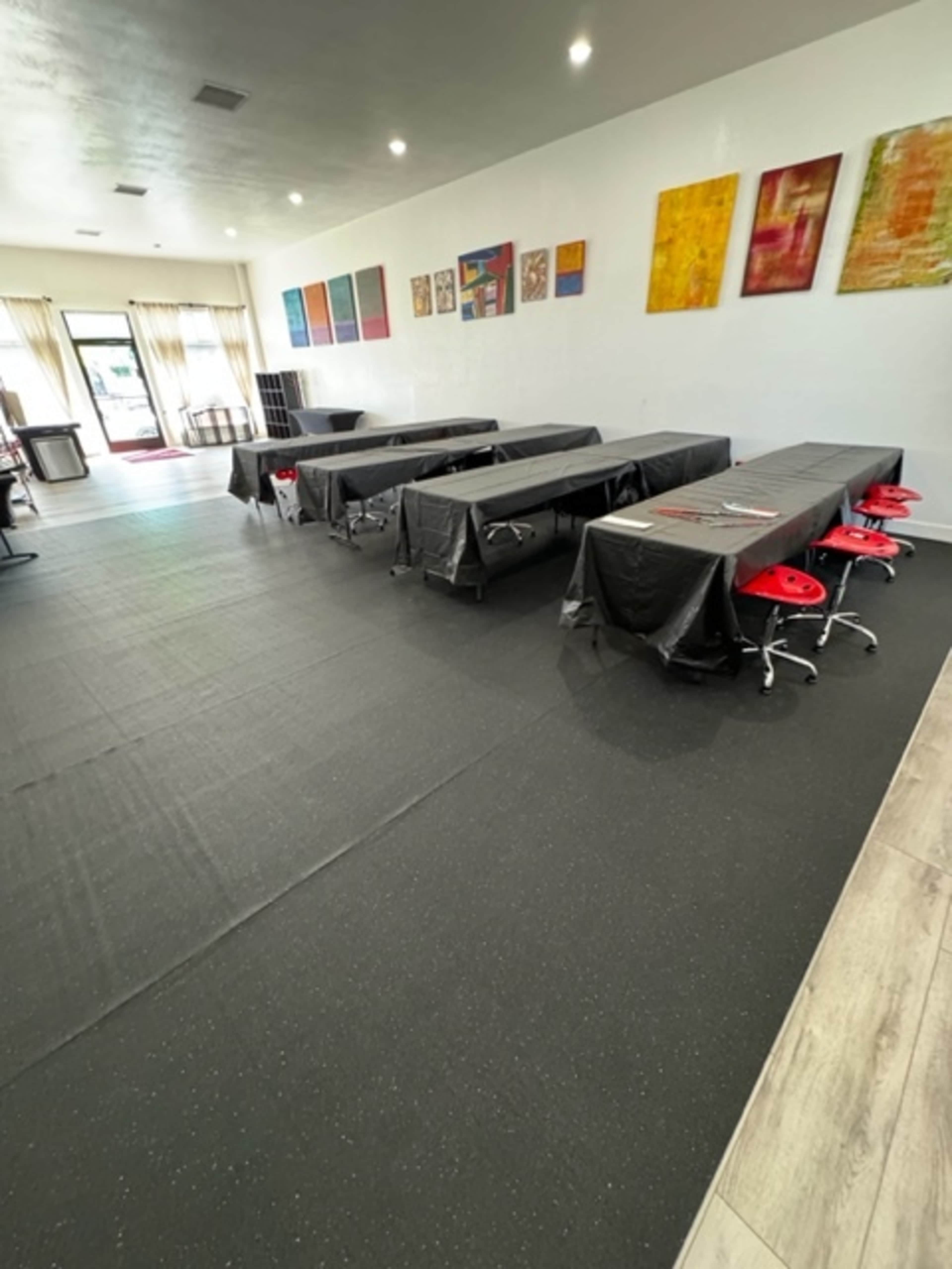 A spacious room with several long tables covered in black cloth, red chairs arranged around them, and colorful artwork on the walls.
