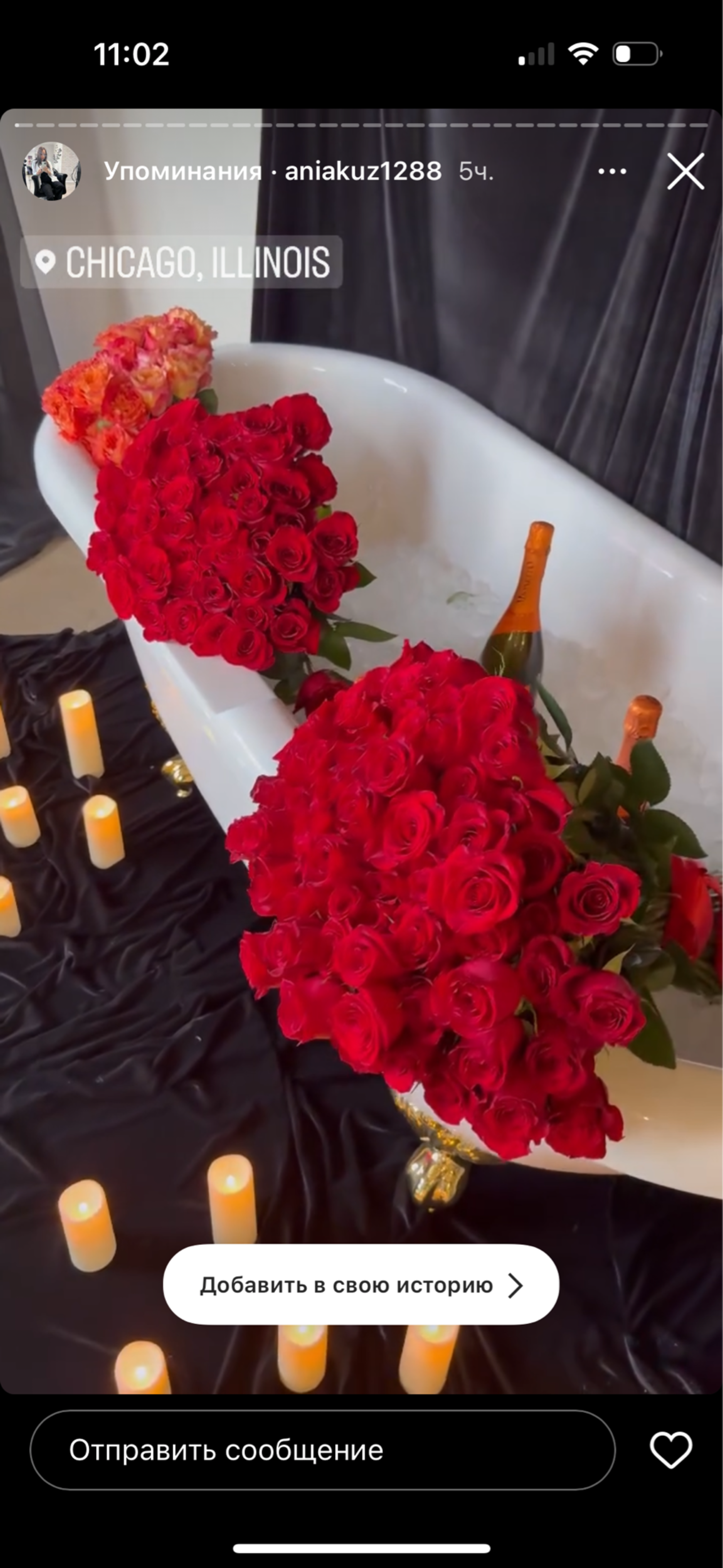 A bathtub filled with water is surrounded by large bouquets of red roses, champagne bottles, and lit candles on a dark surface in Chicago, Illinois.