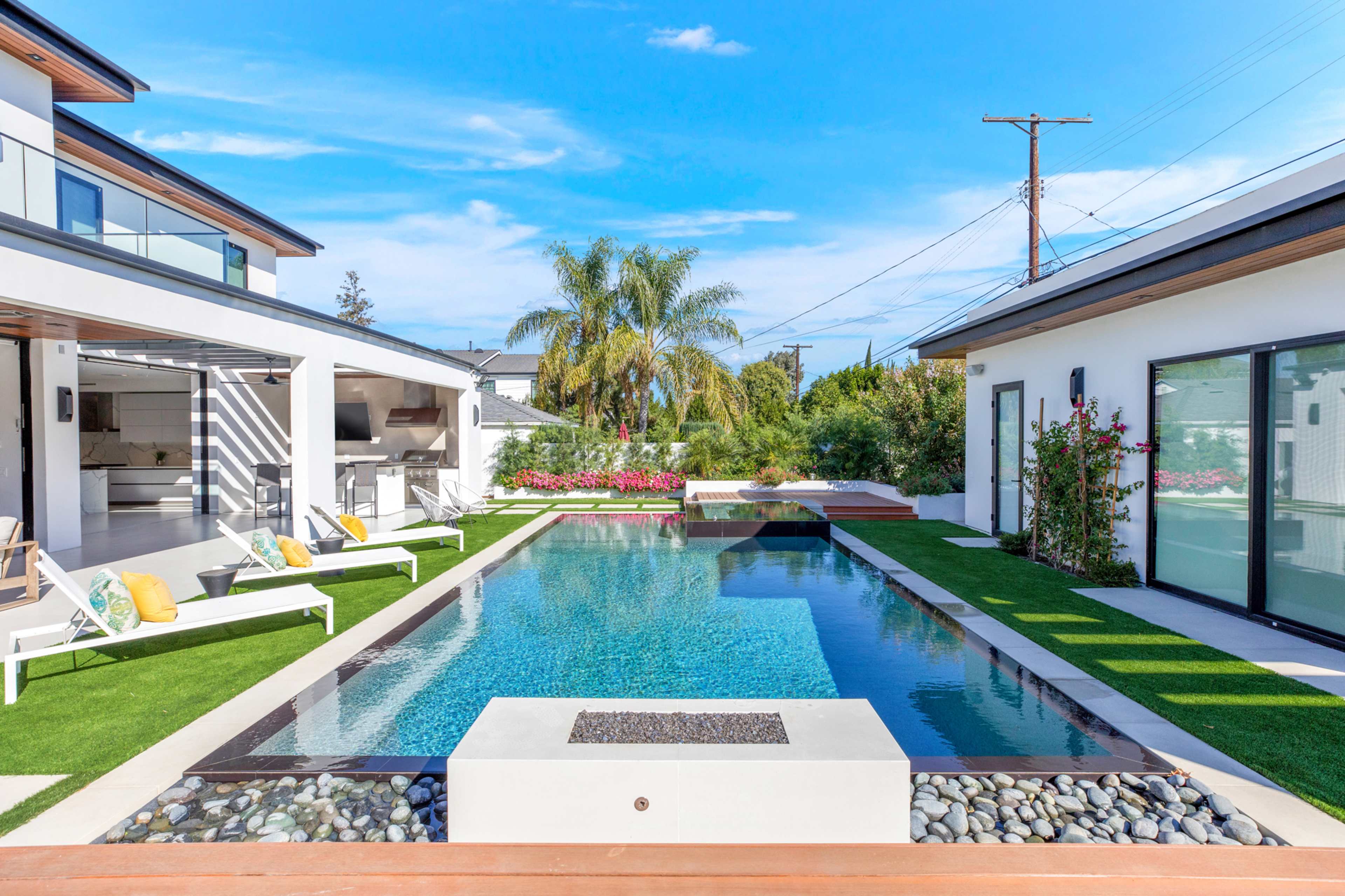 A modern outdoor pool surrounded by landscaped greenery and a spacious patio area with lounge chairs and an outdoor kitchen.