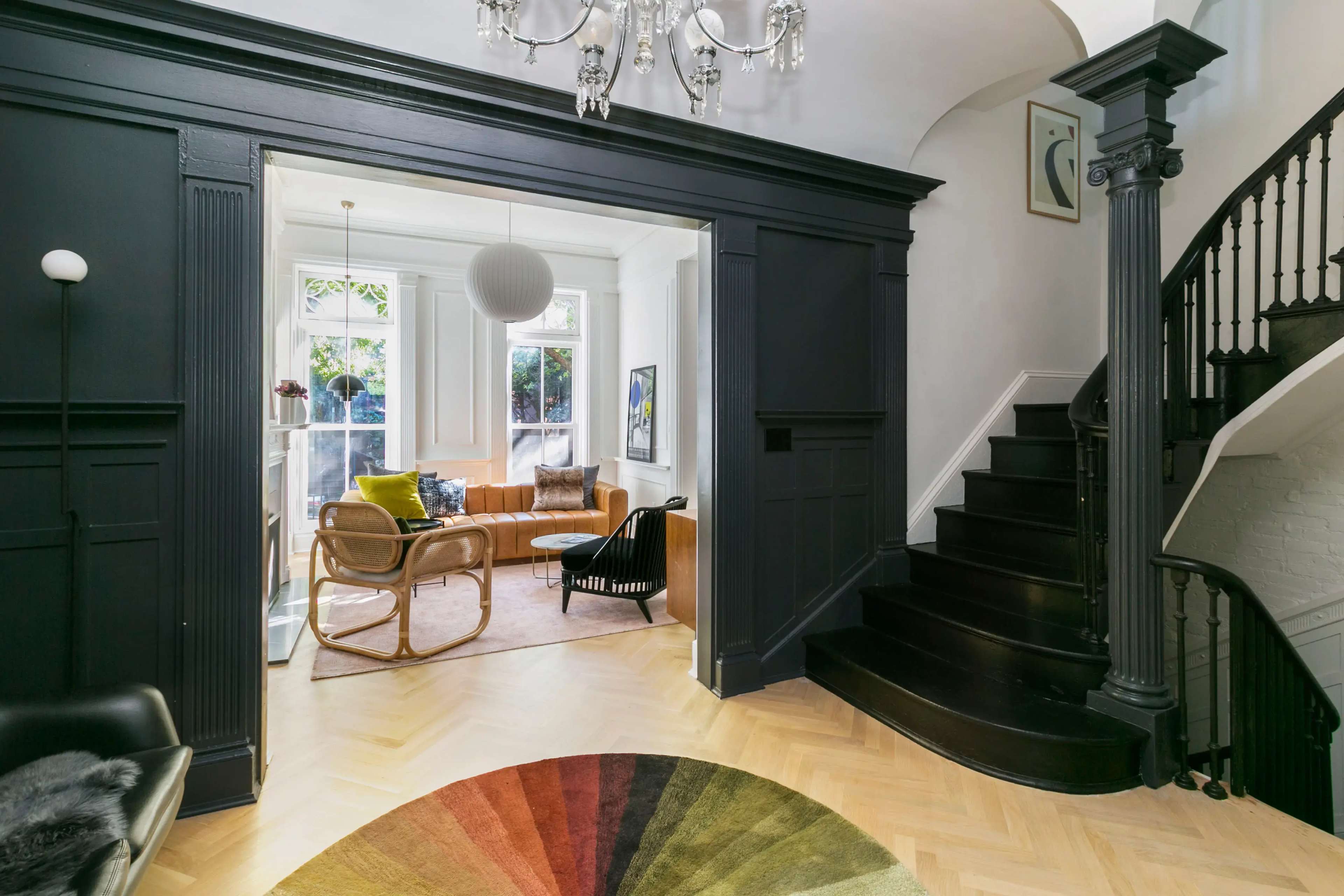 The image shows a stylish entryway leading to a living room with modern furniture and a staircase in a well-lit home.