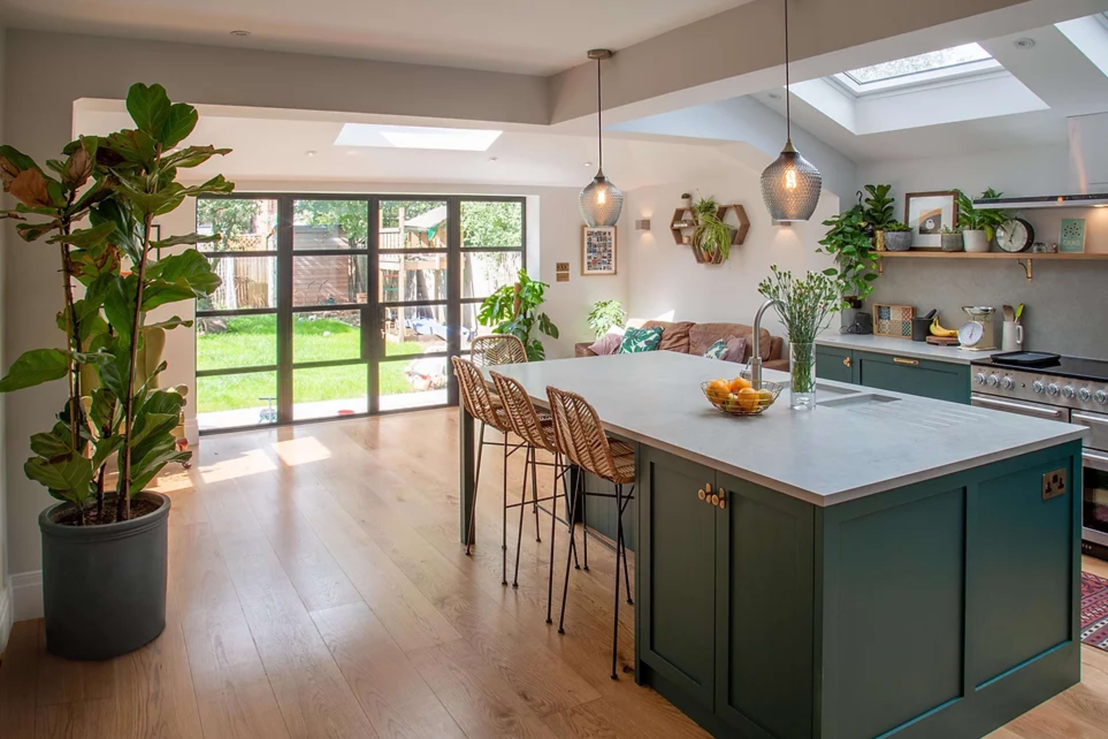 A modern kitchen features an island with bar stools, a sliding glass door opening to a backyard, and ample sunlight streaming through the skylights.