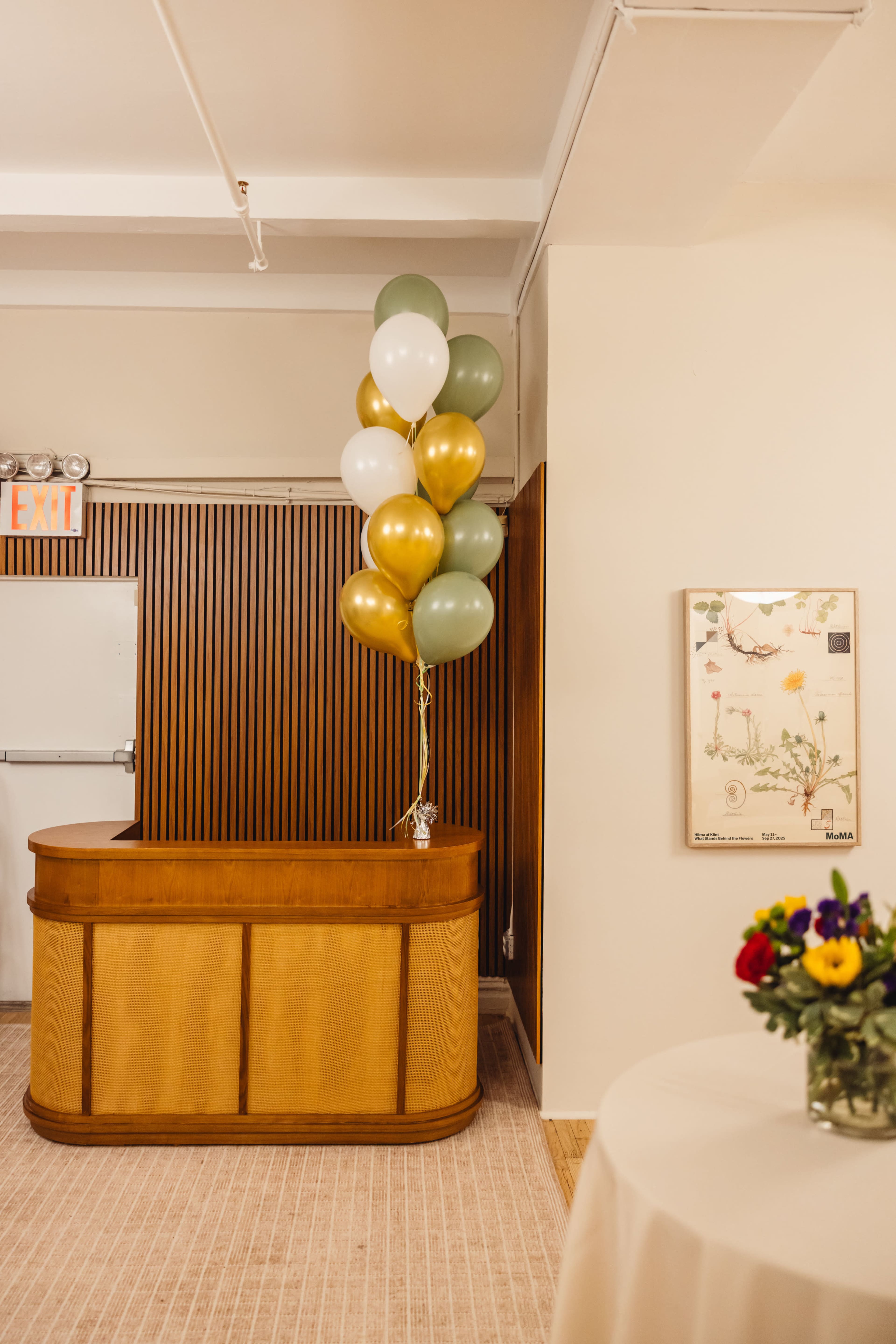A reception area features a wooden front desk with a cluster of balloons in green, gold, and white nearby.
