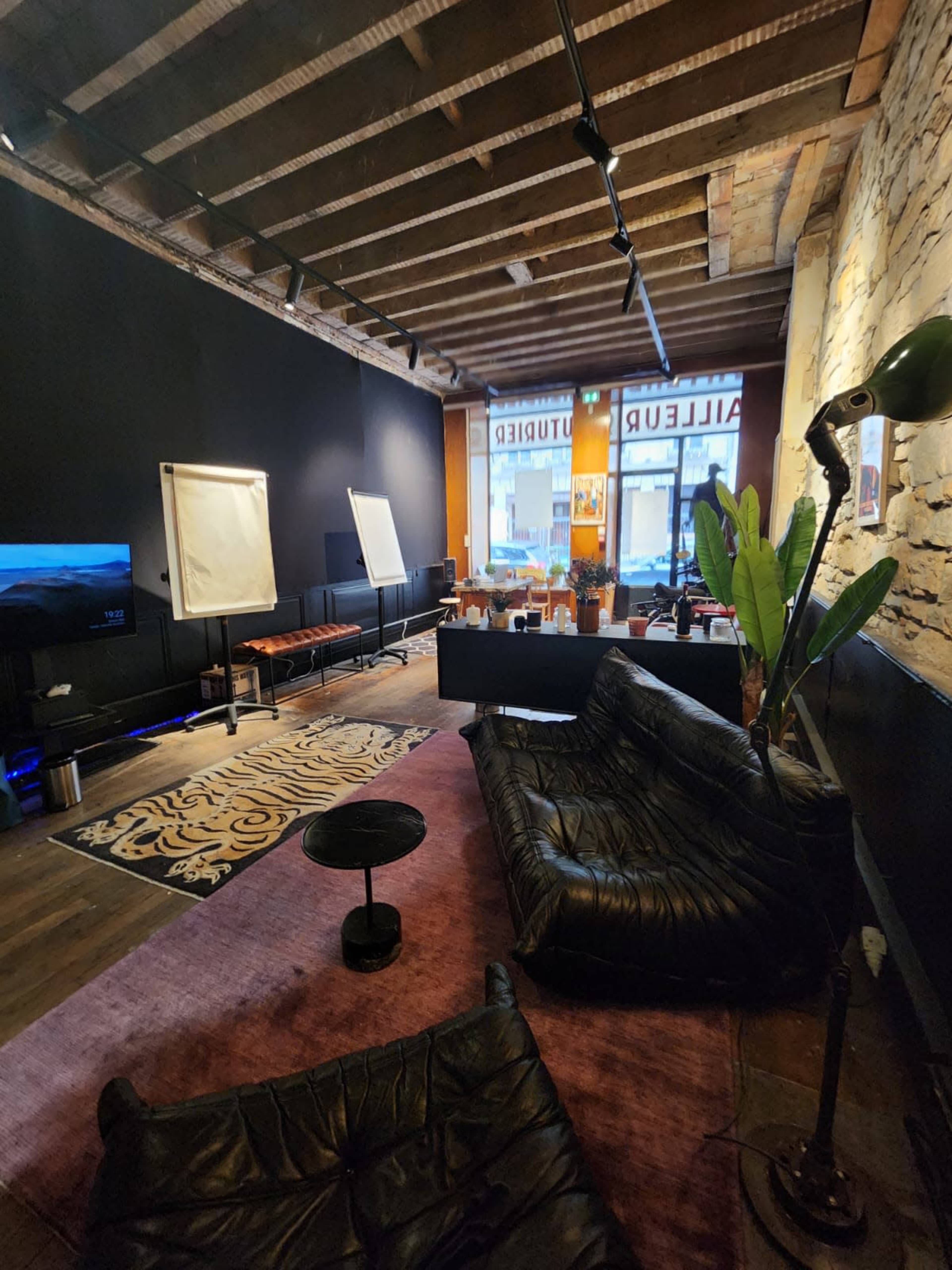 A modern office space with dark walls, leather couches, a coffee table, and a large window displaying a street view.