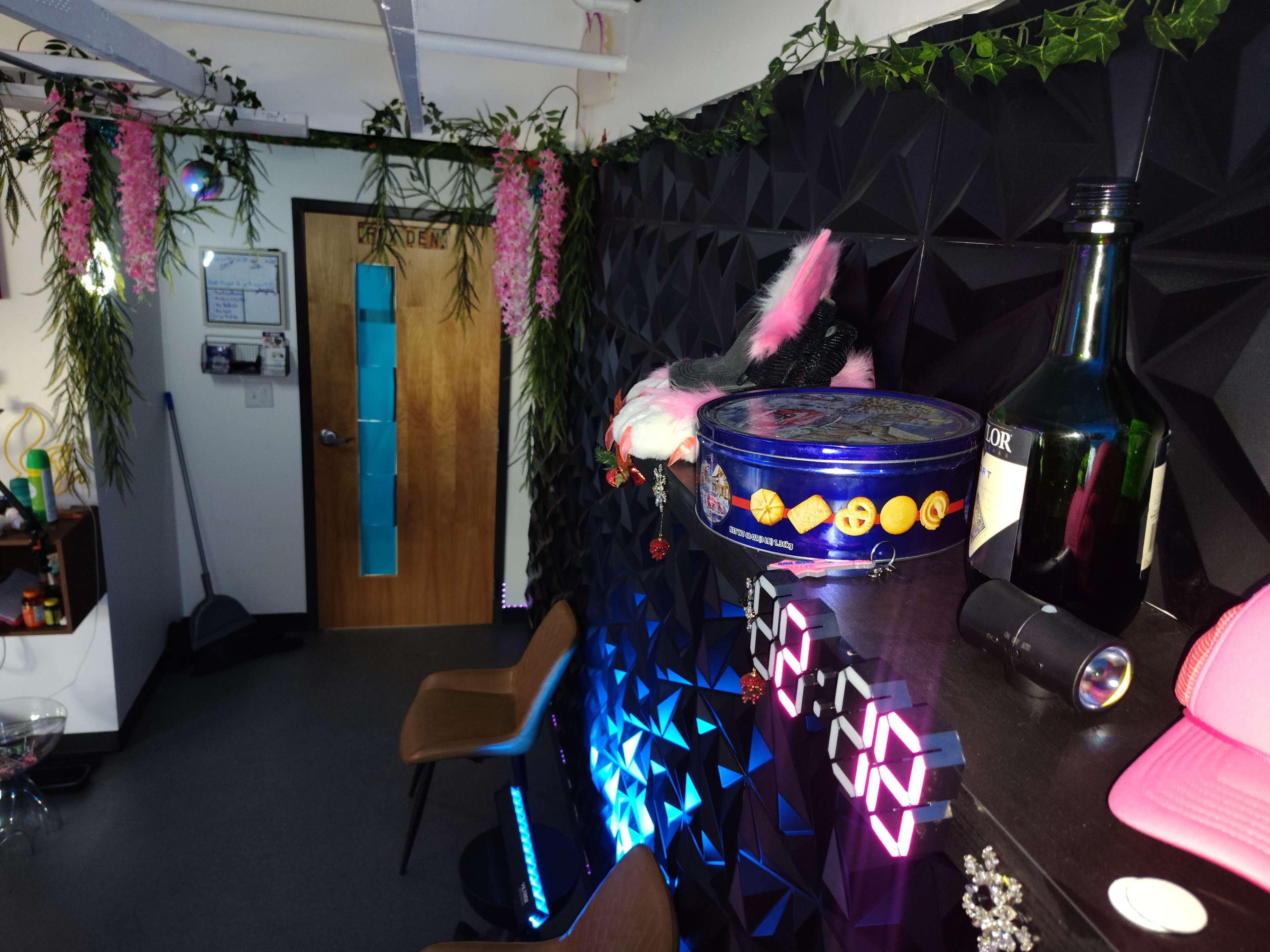 The scene shows a decorated indoor space with a geometric black wall, a door labeled "OFFICE," and various decorations including plants, a bottle, and a canister on a shelf.